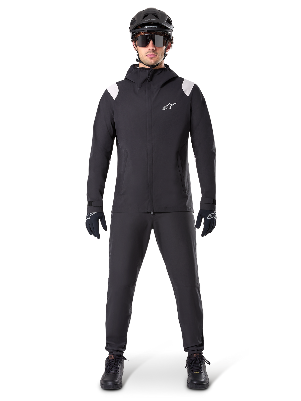 Alpinestars A-Dura Regenjacke, Mountainbike-Regenjacke, Schwarz mit weißen Schulterakzenten und weißem Logo auf der Brust, getragen mit schwarzer Hose, schwarzem Helm, Sonnenbrille und Handschuhen, abgestimmte Mountainbike-Ausrüstung für nasses Wetter