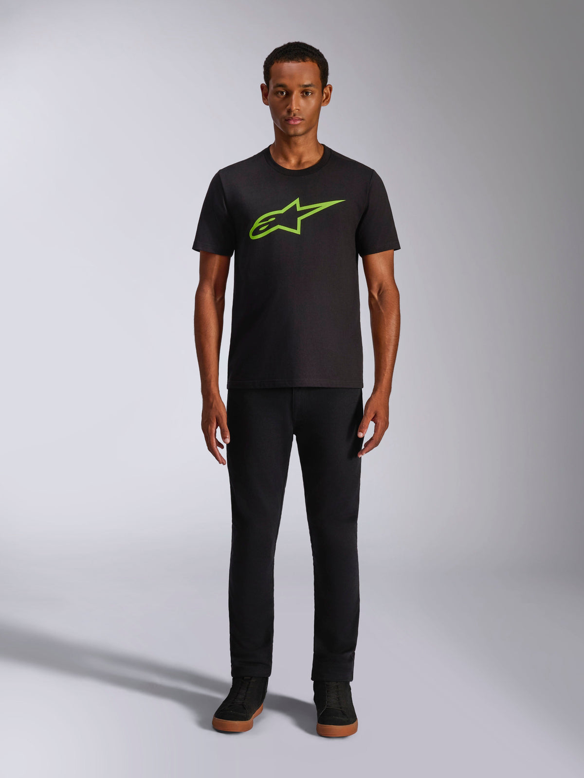 Alpinestars Ageless 2.0 CSF Tee, kurzärmeliges T-Shirt, Schwarz mit hellgrünem Logo, getragen von einem Model mit schwarzer Hose, lässiges, vom Motorsport inspiriertes Design