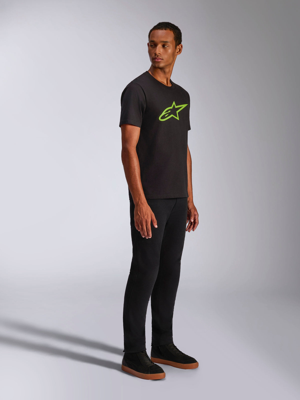 Alpinestars Ageless 2.0 CSF Tee, Kurzarm-T-Shirt, Schwarz mit leuchtend grünem Alpinestars Logo, kombiniert mit schwarzer Hose und Sneakern, lässige vom Motorsport inspirierte Streetwear