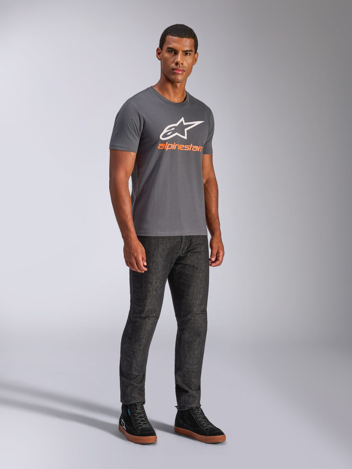 Alpinestars Always 2.0 CSF Tee, Kurzarm-T-Shirt, Anthrazitgrau, weißes A-Star-Logo mit orangefarbenem Branding, lässige Motorsport-Streetwear kombiniert mit dunkler Jeans und schwarzen Sneakern