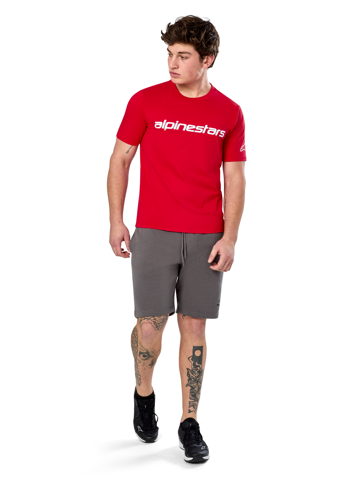 Alpinestars Linear Wordmark 2.0 CSF Tee, kurzärmeliges T-Shirt, Rot mit weißem Logo-Schriftzug auf der Brust, getragen von einem Model mit grauen Shorts und schwarzen Sneakern, lässige vom Motorsport inspirierte Streetwear