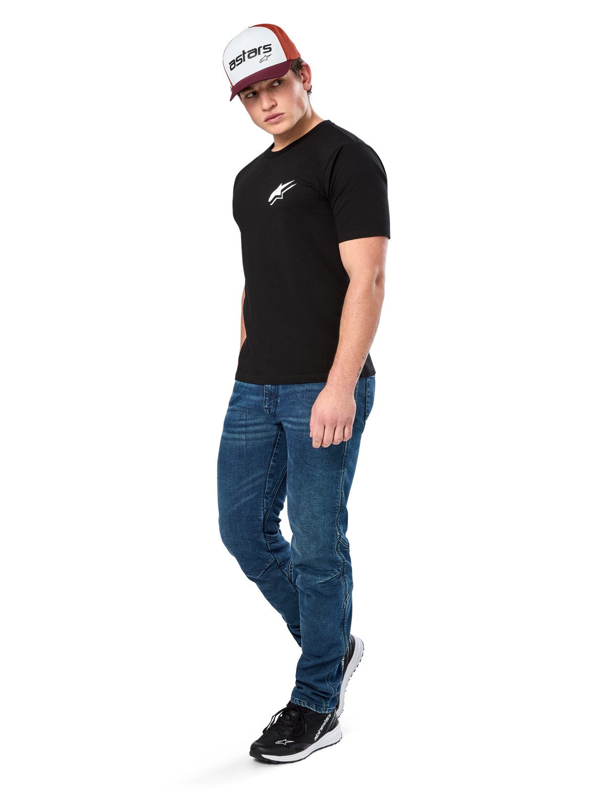 Alpinestars Formulate Csf Tee, Kurzarm-T-Shirt, Schwarz mit weißem Astars-Logo auf der Brust, getragen von einem Model mit blauen Jeans, einer bordeauxroten und weißen Kappe und schwarzen Sneakern, lässige, vom Motorsport inspirierte Streetwear