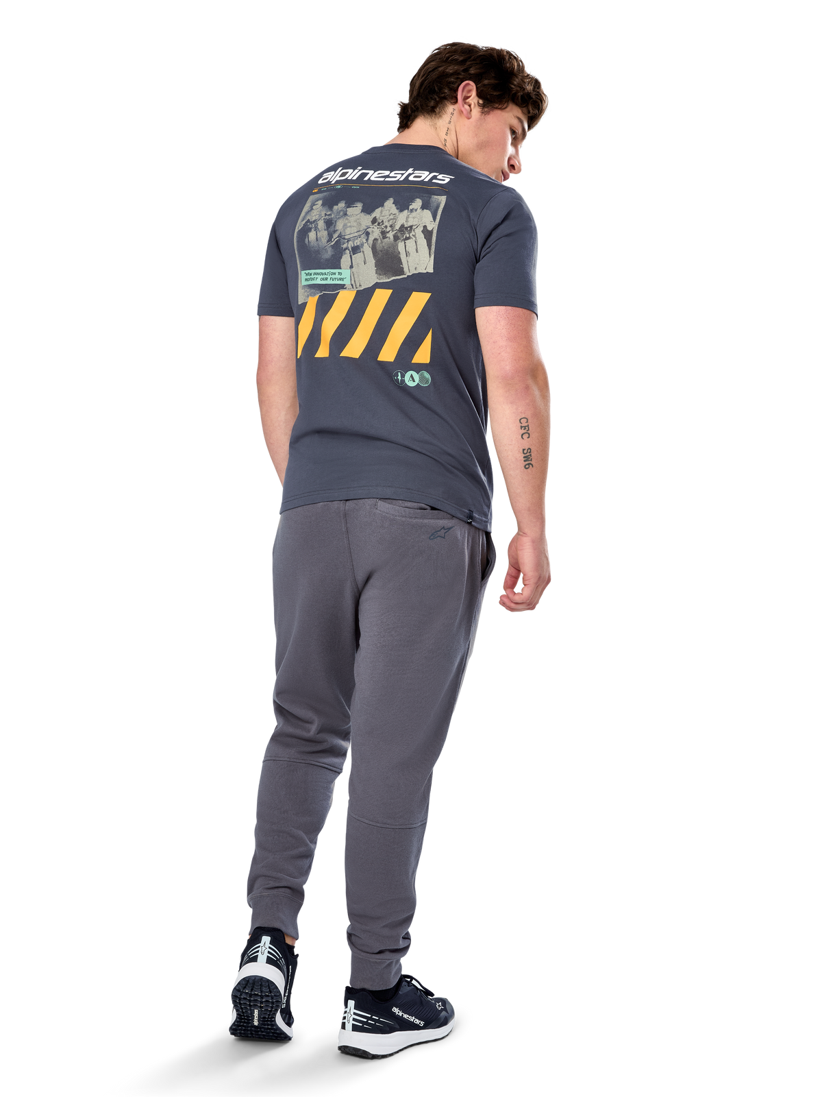 Alpinestars No Barrier CSF Tee, kurzärmeliges T-Shirt, Anthrazit, Rückansicht mit großer Distressed-Fotografik, gelben diagonalen Streifen und weißem Logo, lässige, vom Motorsport inspirierte Streetwear