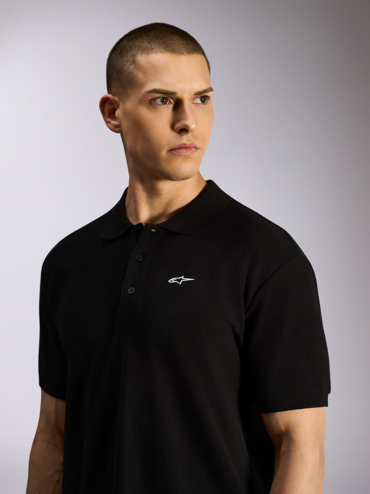 Alpinestars Endeavor Classic Polo, schwarzes Piqué-Poloshirt getragen von einem männlichen Model, kleines weißes Astars-Logo auf der Brust, 3-Knopf-Leiste und Rippkragen, lässige Motorsport-Streetwear