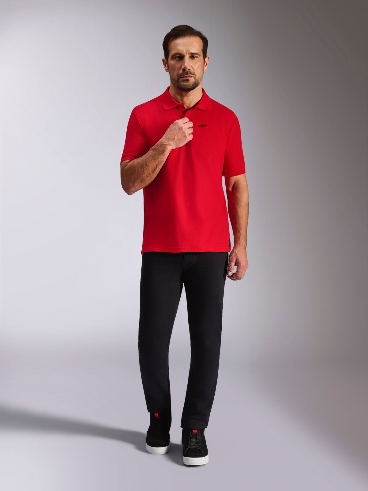 Alpinestars Endeavor Classic Polo, rotes Piqué-Poloshirt, Kurzarm mit schwarzem Astars-Logo, gerippter Kragen und Ärmelbündchen, getragen mit schwarzer Hose und Sneakern, lässige motorsport-inspirierte Streetwear