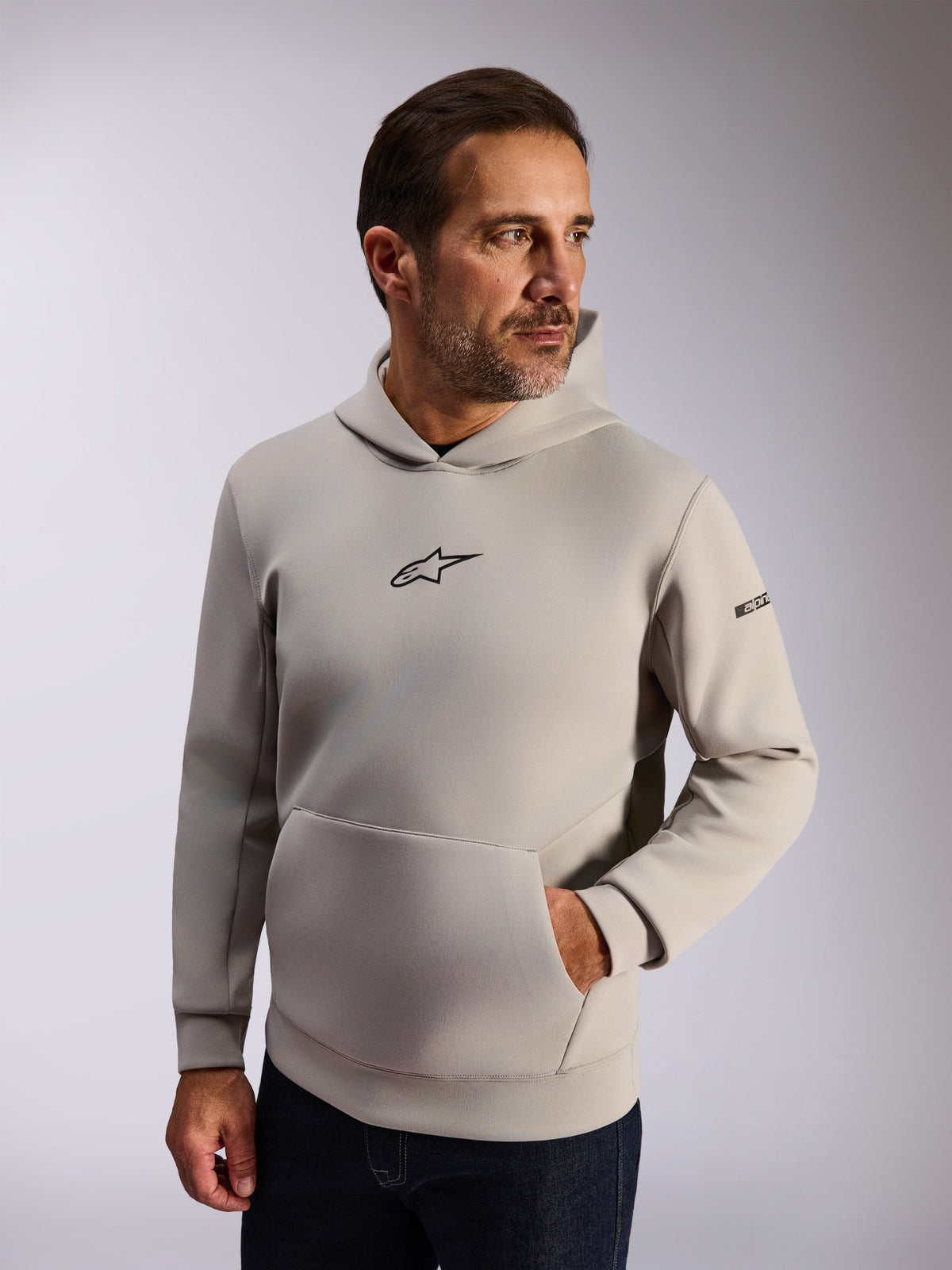 Alpinestars Insight Kapuzenpullover, lässige Lifestyle-Streetwear, zementgraues Fleece, schwarzes Astars-Logo auf der Vorderseite, Kängurutasche, Wortmarke am Ärmel, Kapuze mit Mesh-Futter, moderne vom Motorsport inspirierte Bekleidung
