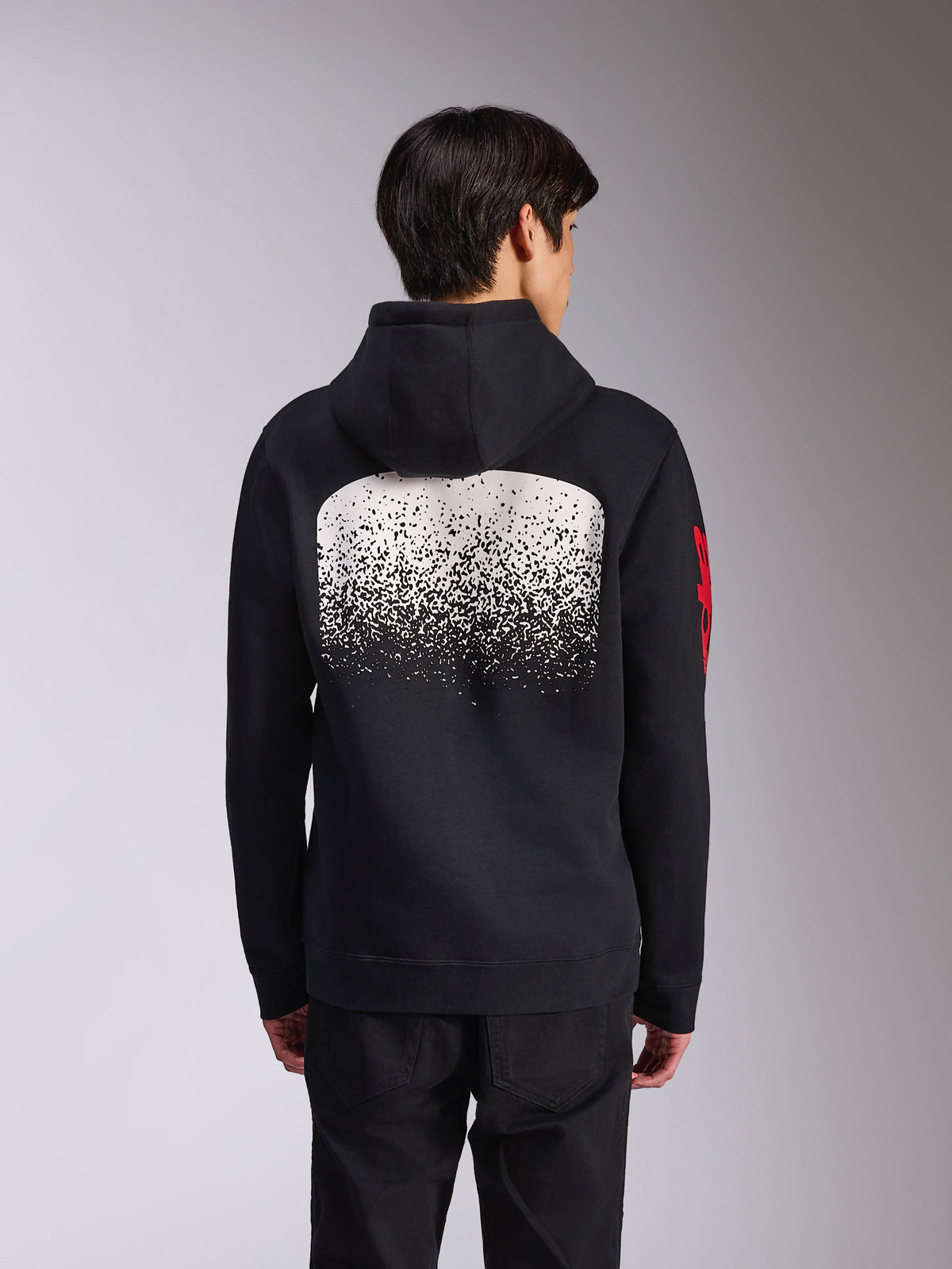 Alpinestars Obsessed Hoodie, Rückansicht eines schwarzen Fleece-Kapuzenpullovers, mit einer großen weiß gesprenkelten MX-Grafik mit Farbverlauf auf dem Rücken und roten Alpinestars-Wortlogos auf den Ärmeln, lässige, vom Motorsport inspirierte Streetwear