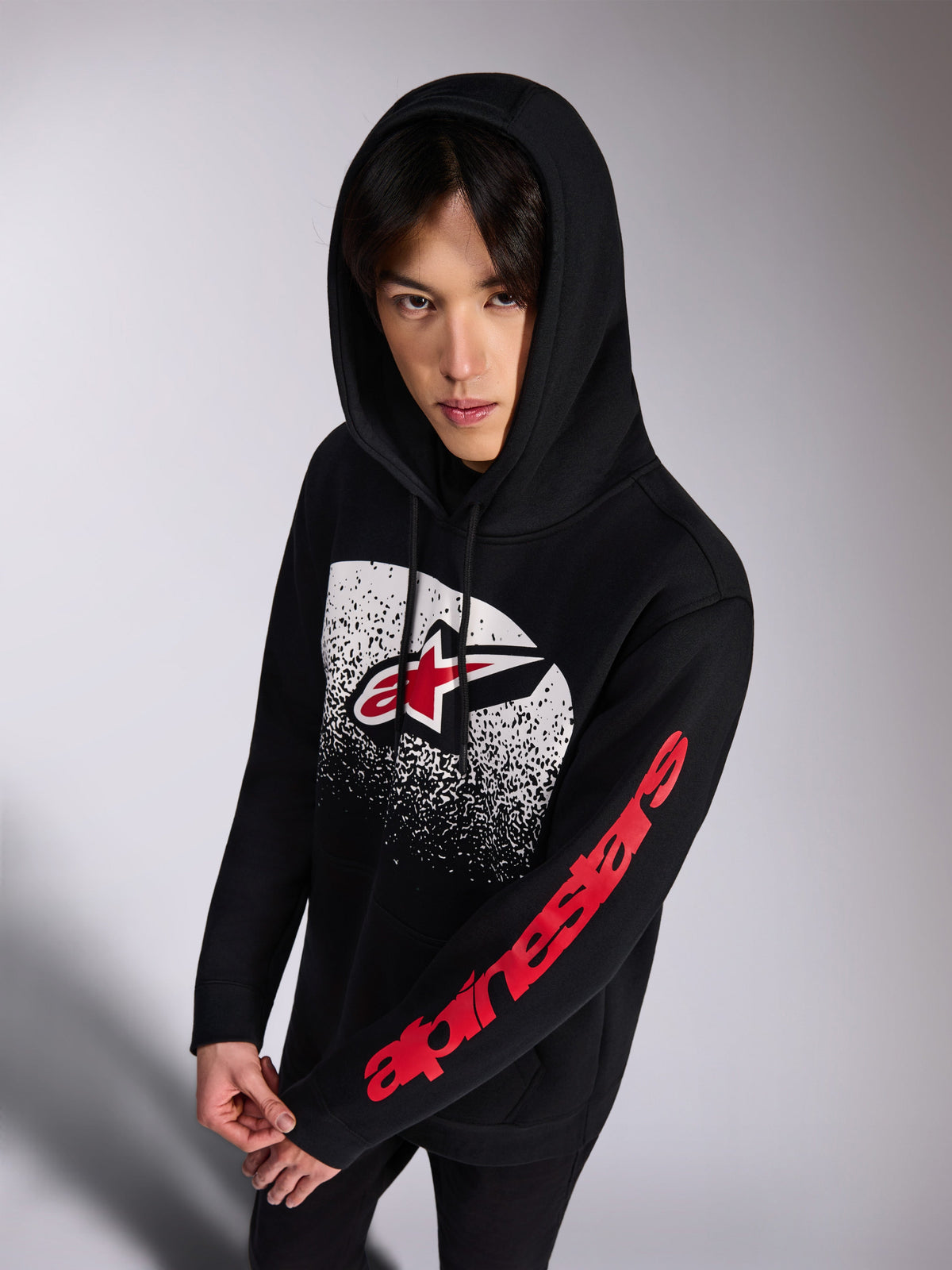 Alpinestars Obsessed Hoodie, schwarzer Kapuzenpullover aus Fleece, rotes und weißes Astars-Logo vorne mit weißem MX-Farbverlauf im Distressed-Look, roter Alpinestars-Schriftzug am Ärmel, Kapuze mit Kordelzug, lässige Motorsport-inspirierte Streetwear
