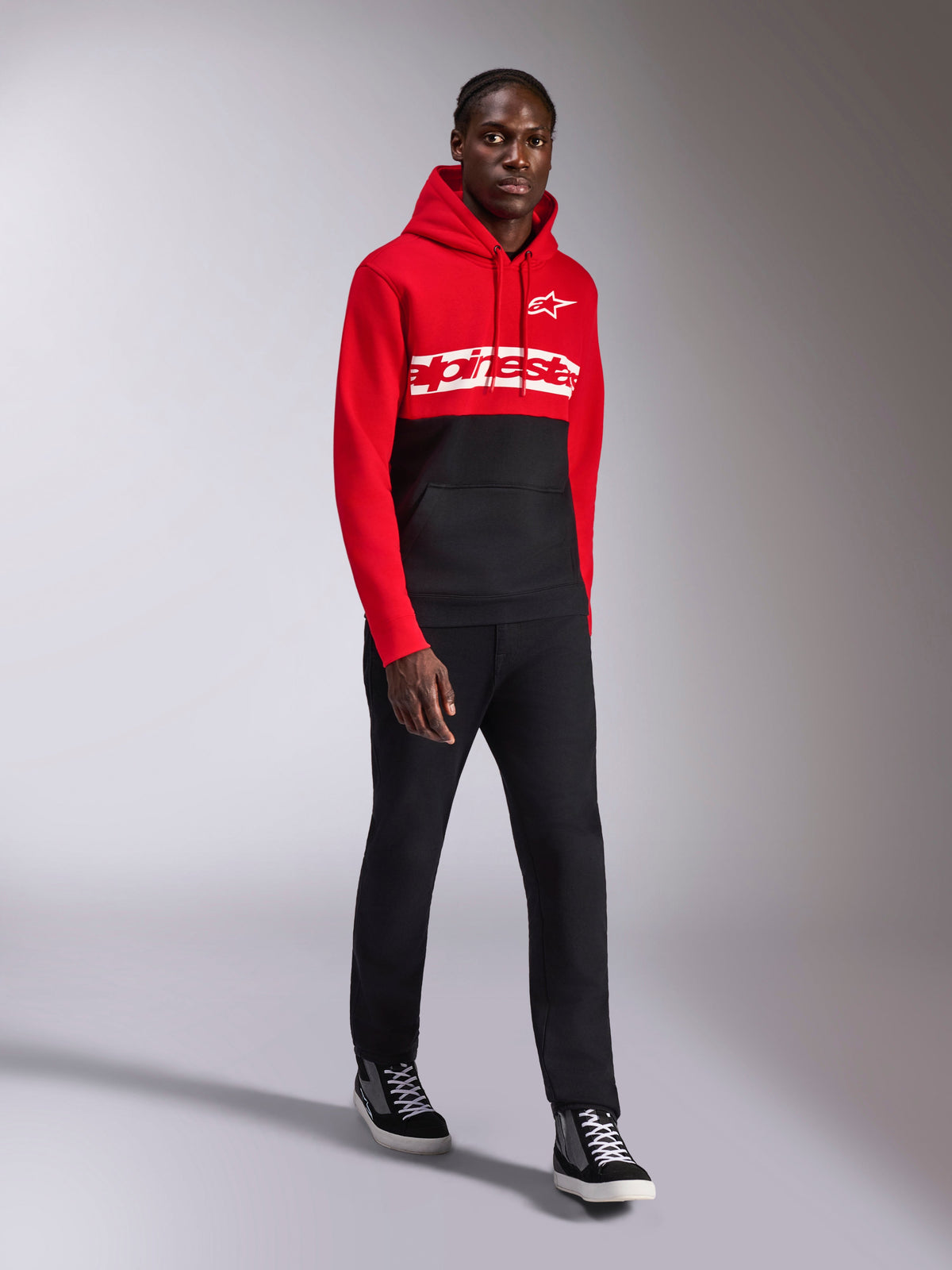 Alpinestars Parallel Hoodie, lässige Sportbekleidung, rot-schwarzes Color-Block-Design, weißer Alpinestars-Schriftzug und Stern-Logo auf der Brust, kombiniert mit schwarzer Hose und Sneakern, moderner, vom Motorsport inspirierter Look