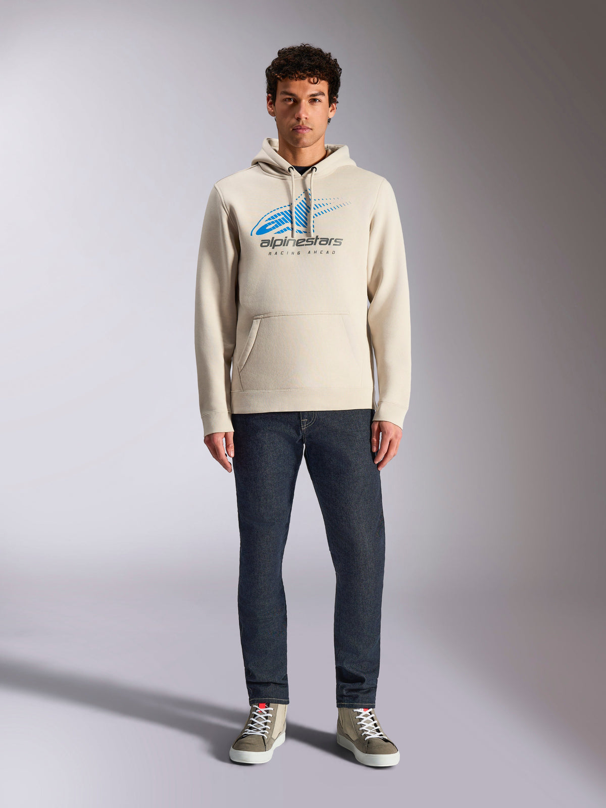 Alpinestars Pulse Hoodie, Off White, long sleeve pullover with drawstring hood, blue and black Astars Combo Logo with speed line fade, styled with dark jeans and sneakers, casual motorsport streetwear
