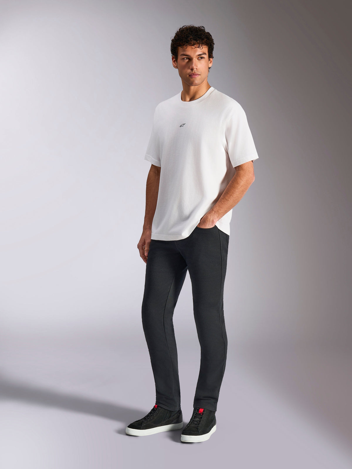 Alpinestars Focused Oversized CSF Tee, Kurzarm-T-Shirt, Weiß, mit kleinem schwarzen Astars-Logo auf der Brust, getragen von einem männlichen Model mit dunkler Hose und schwarzen Sneakern, lässige, vom Motorsport inspirierte Streetwear