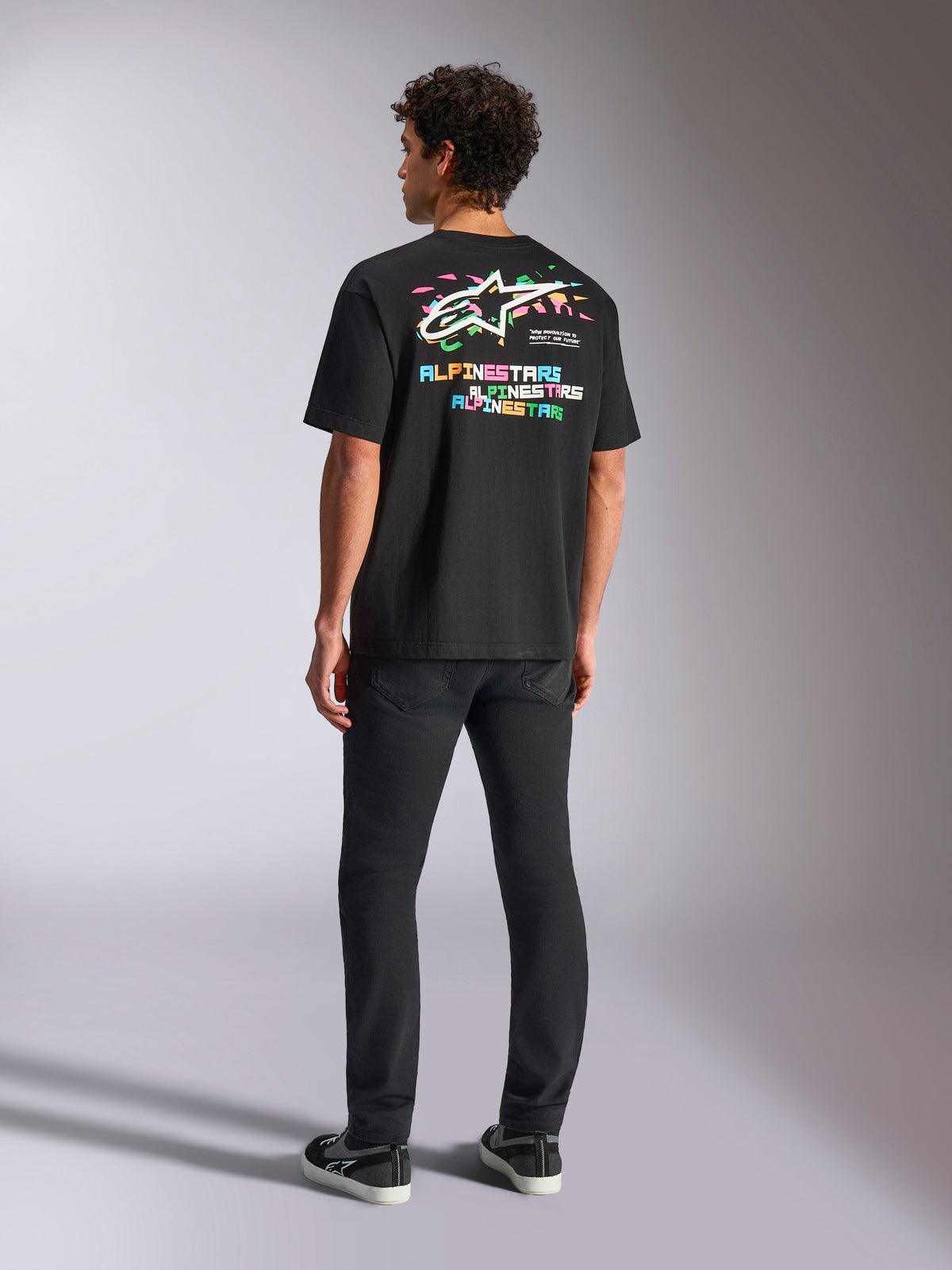 Alpinestars Wild Oversized CSF Tee, Short Sleeve T-Shirt, Black, featuring a large multi-color back graphic with Astars logo and colorful lettering, oversized fit, worn with black slim-fit pants for a casual streetwear look