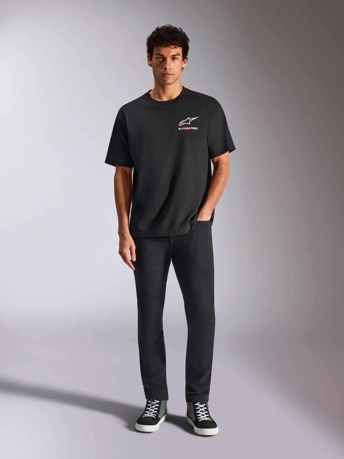 Alpinestars Wild Oversized CSF Tee, Short Sleeve T-Shirt, Black, worn by a model with black trousers and sneakers, featuring a white Astars logo and vibrant multi-color branding, casual motorsport streetwear