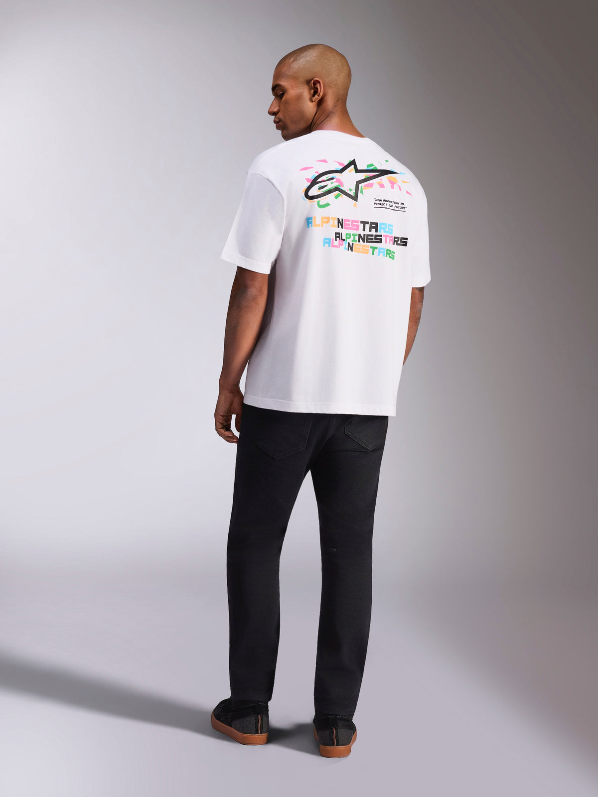 Alpinestars Wild Oversized CSF Tee, Kurzarm-T-Shirt, Weiß, Rückansicht eines Modells, das ein Oversized-T-Shirt mit lebhaftem mehrfarbigem Astars-Logo und gestapeltem Text auf der Rückseite trägt, lässige, vom Motorsport inspirierte Streetwear