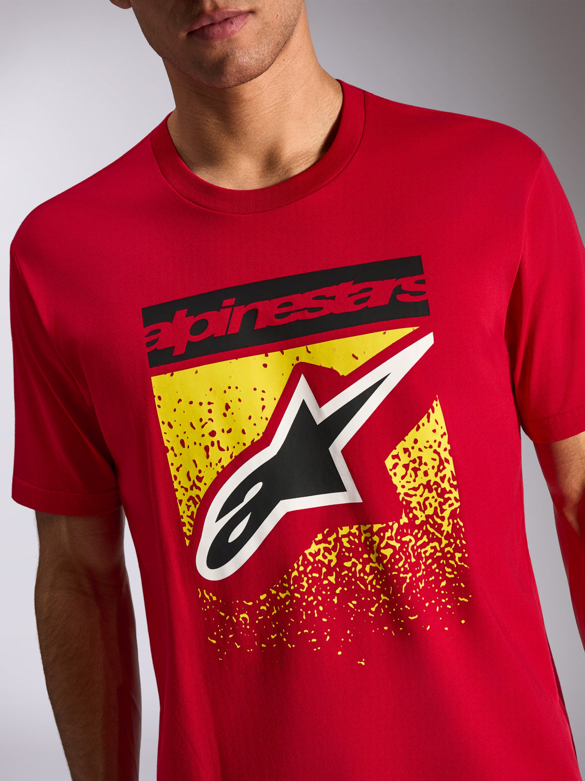 Alpinestars Noka CSF Tee, Kurzärmeliges T-Shirt, Rot, Frontgrafik mit schwarzem Alpinestars-Schriftzug und Astars-Logo auf gelbem, gesprenkeltem Design, Casual Motorsport Streetwear