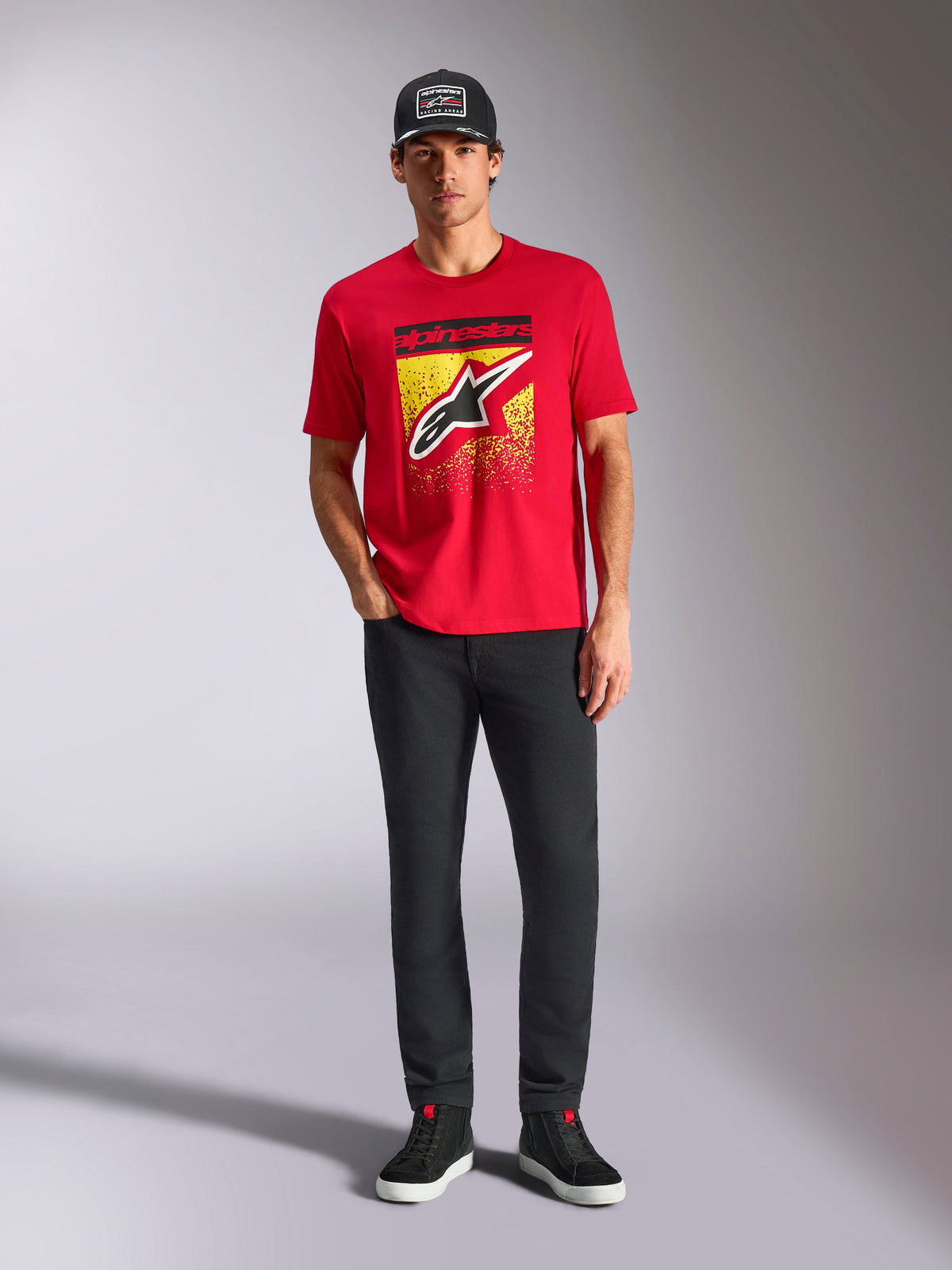 Alpinestars Noka CSF Tee, Kurzarm-T-Shirt, Rot, mit einem großen Astars-Logo auf der Vorderseite mit gelbem und schwarzem MX-Farbverlauf, getragen mit schwarzer Hose und schwarzer Kappe, Casual Motorsport Streetwear
