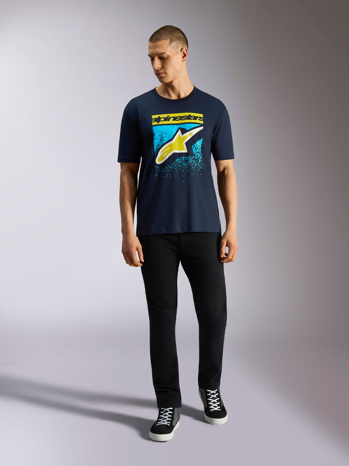 Alpinestars Noka CSF Tee, Kurzarm-T-Shirt, Navy-Blau, Astars-Logo vorne mit gelbem und hellblauem MX-Farbverlauf, getragen von einem Model mit schwarzer Hose, lässige Motorsport-Streetwear