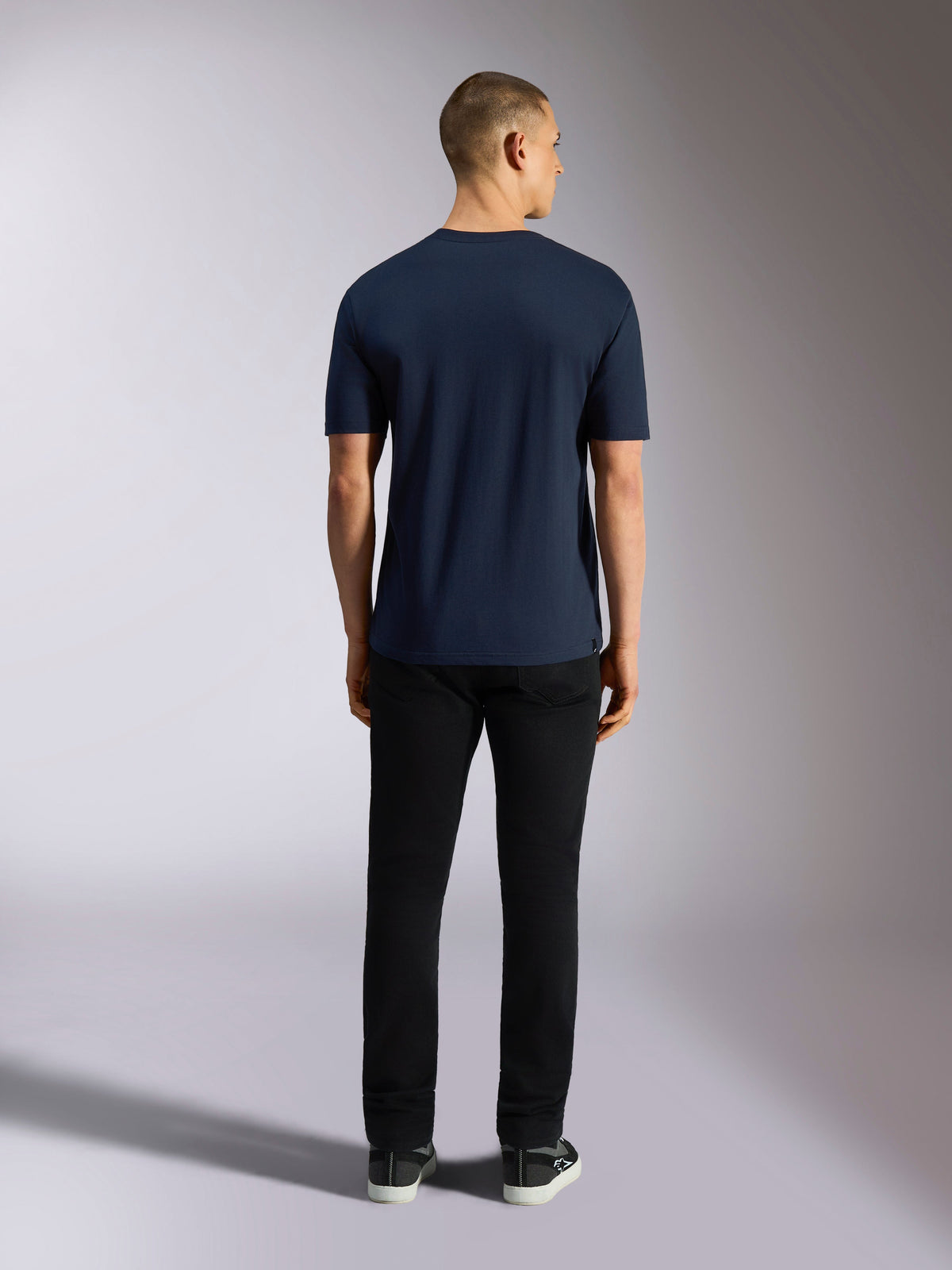 Alpinestars Noka CSF T-Shirt, kurzärmliges T-Shirt, Marineblau, Rückansicht eines Mannes in schwarzer Hose und Sneakern, lässige Motorsport-Streetwear