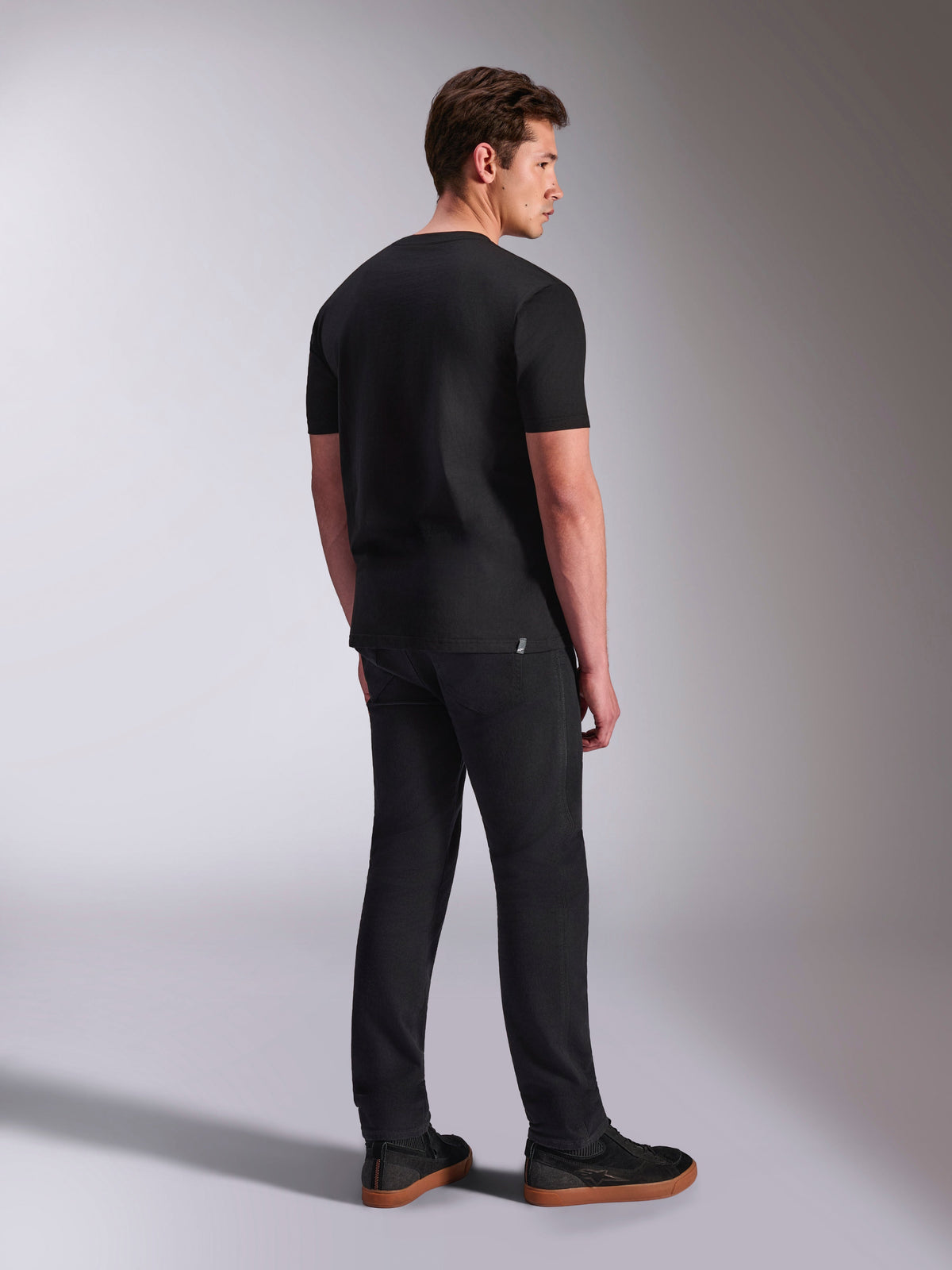 Alpinestars Abus CSF Tee, kurzärmeliges T-Shirt, Schwarz, Rückansicht an einem männlichen Model, lässige Motorsport-Streetwear, kombiniert mit dunkler Hose und Sneakern