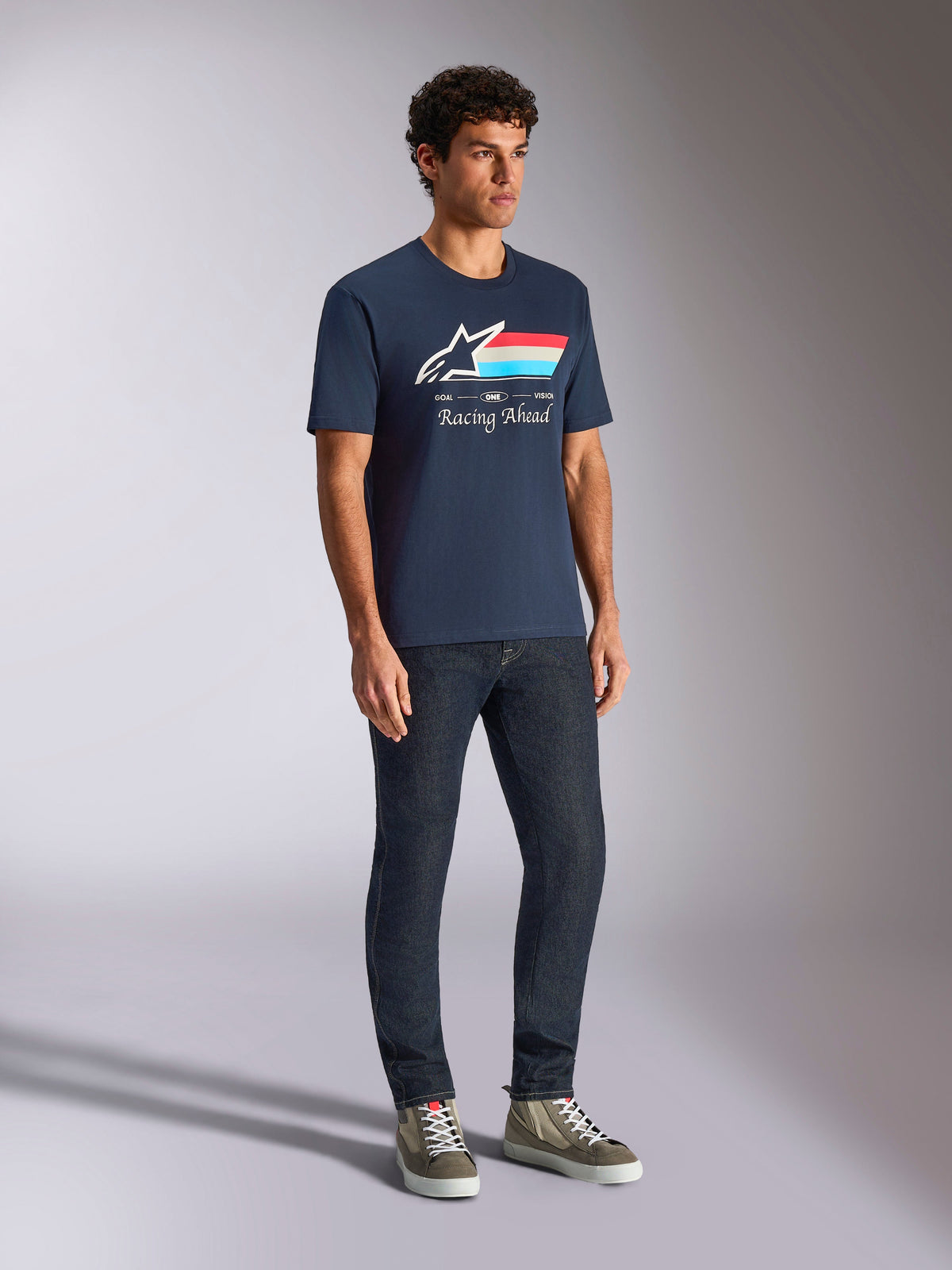 Alpinestars Trifecta CSF Tee, Short Sleeve T-Shirt, Navy Blue, featuring Astars logo with tri-color stripes and Racing Ahead text, worn by a model with dark jeans and sneakers, casual motorsport-inspired streetwear