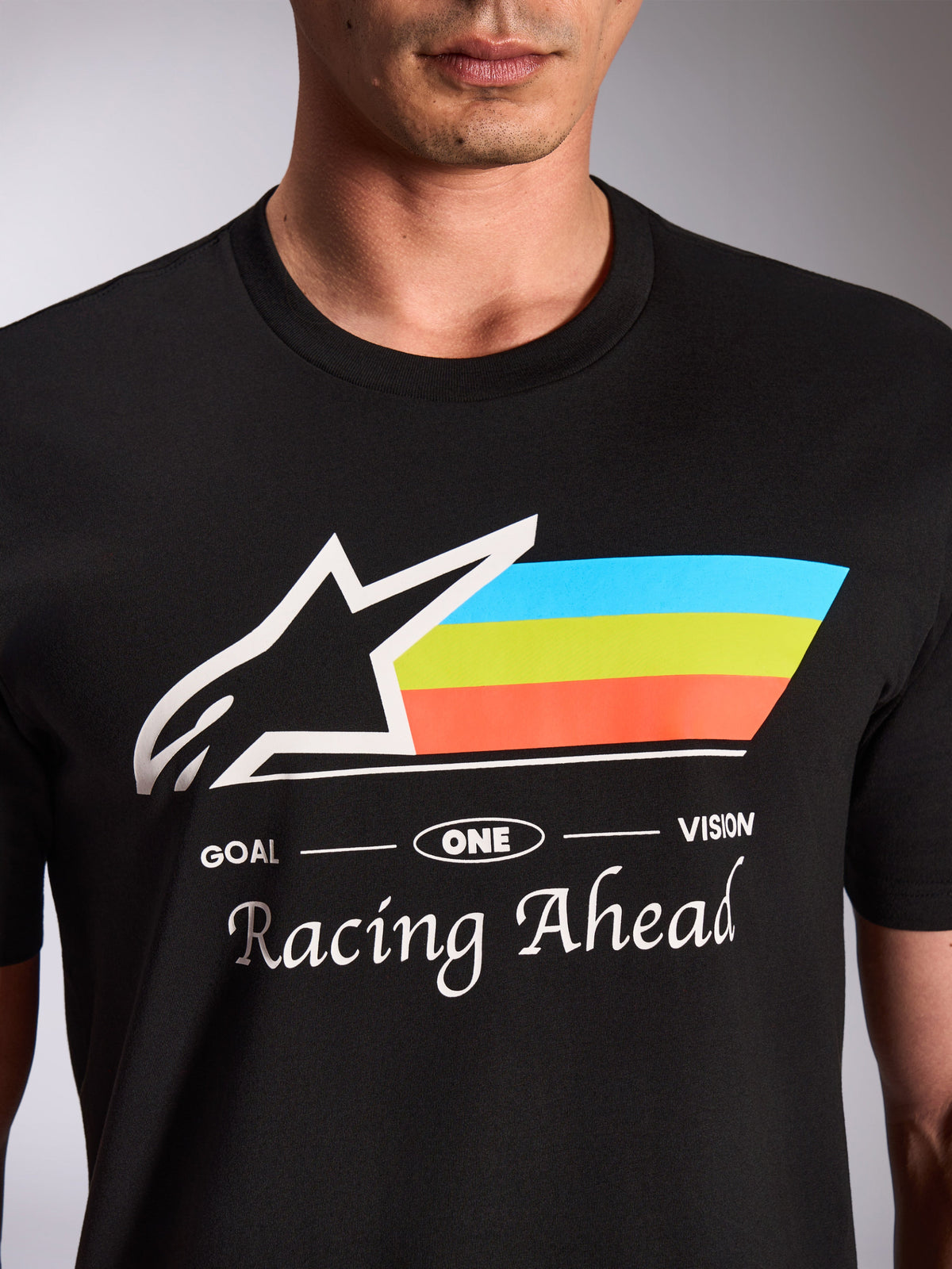 Alpinestars Trifecta CSF Tee, kurzärmeliges T-Shirt, Schwarz, Nahaufnahme der Frontgrafik mit weißem Astars-Logo und dreifarbigen Streifen in Blau, Grün und Orange, 'Racing Ahead'-Schriftzug, lässige Motorsport-Streetwear