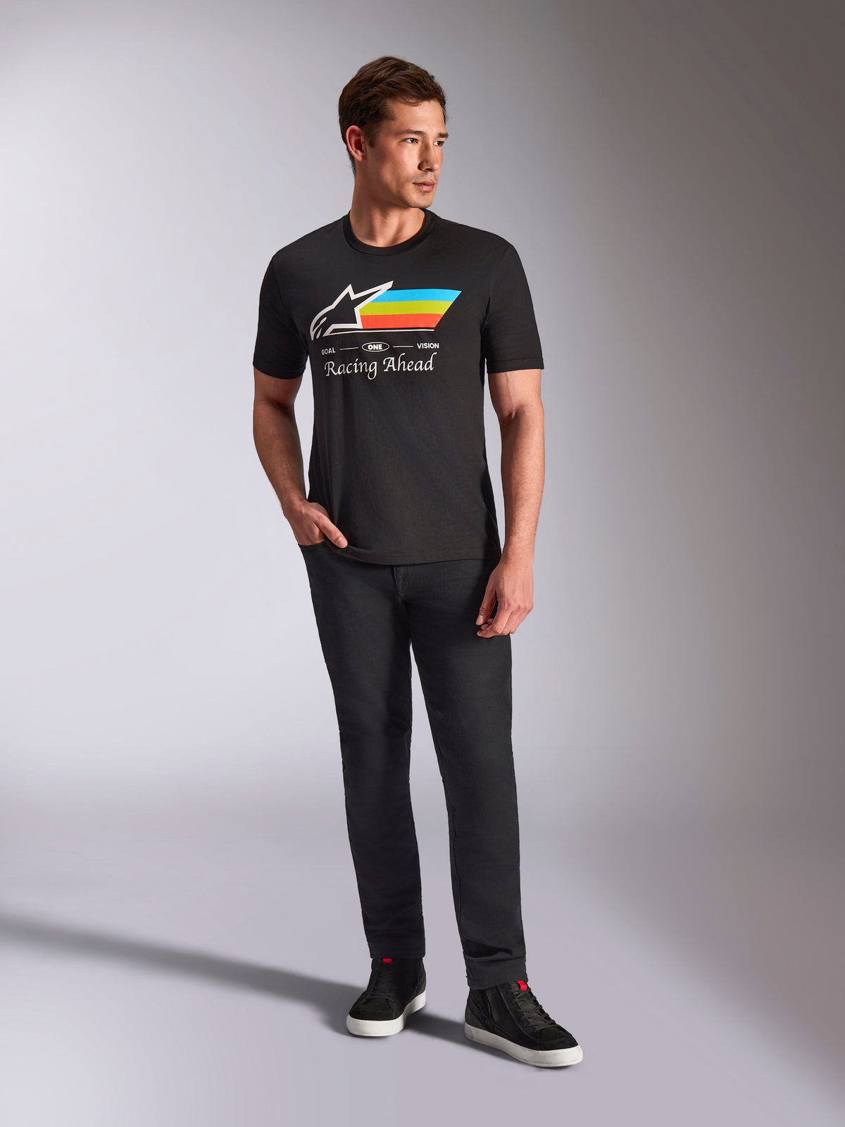 Alpinestars Trifecta CSF T-Shirt, kurzärmeliges T-Shirt, Schwarz, mit weißem Astars-Logo sowie Streifen in Cyan, Gelb und Orange und dem Schriftzug „Racing Ahead“, getragen von einem Model mit schwarzer Hose und Sneakern für einen lässigen Motorsport-Streetwear-Look.