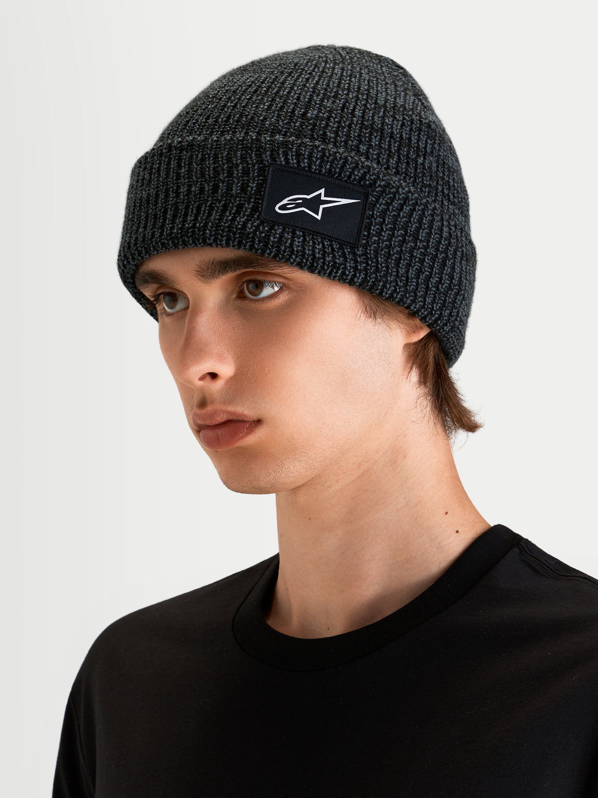 Alpinestars Unload Rib Cuff Mütze, Sportswear-Strickmütze in Anthrazitgrau und Schwarz, an einem Model mit flachem Profil und gewebtem SAstars-Logoaufnäher