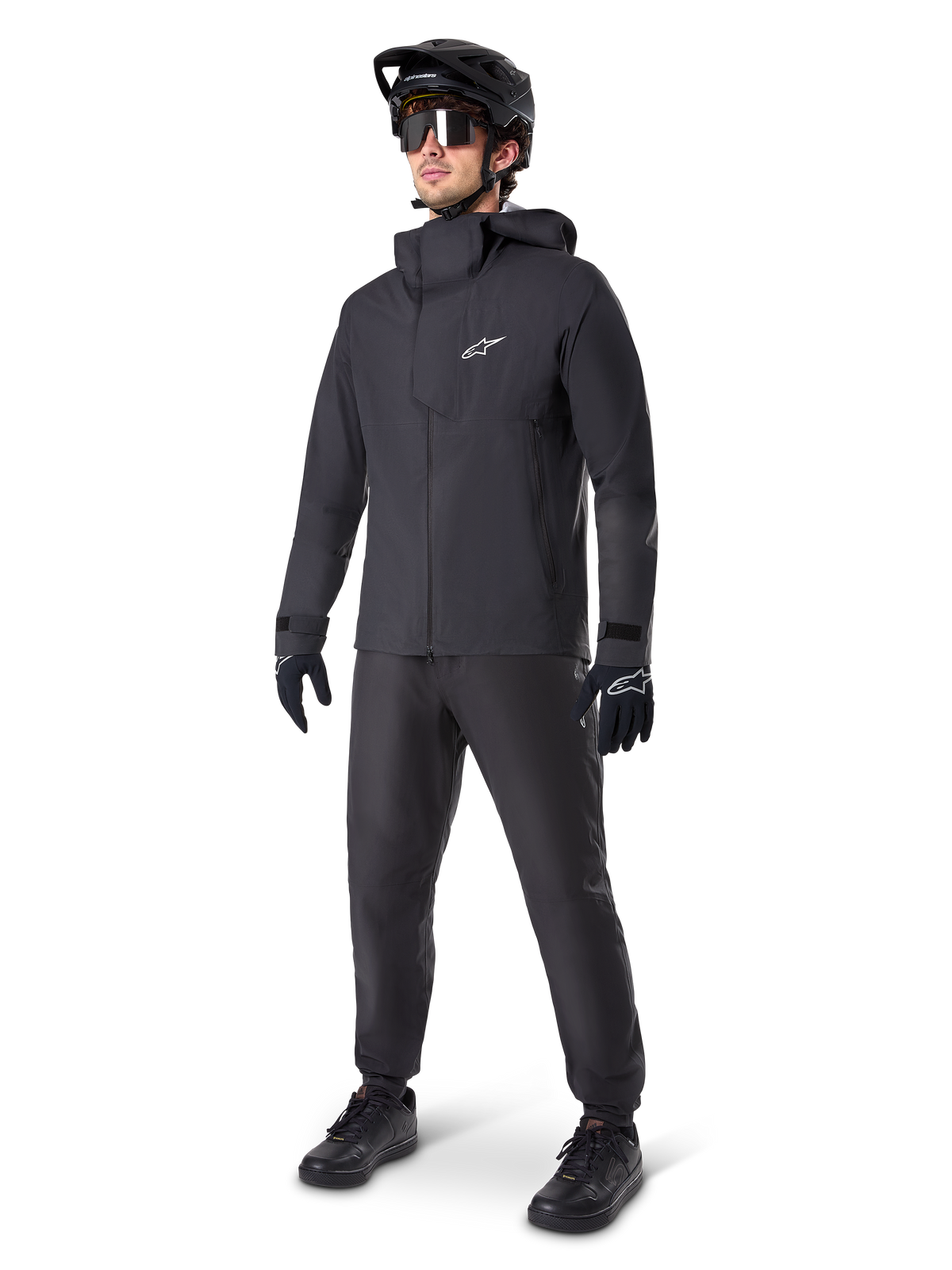 Alpinestars A-Dura Elite Wasserdichte Jacke in Schwarz, getragen von einem männlichen Fahrer mit passender schwarzer MTB-Hose, Handschuhen und Helm, technisches wasserdichtes Design, weißes Astars-Logo auf der Brust, hoher Schutzkragen