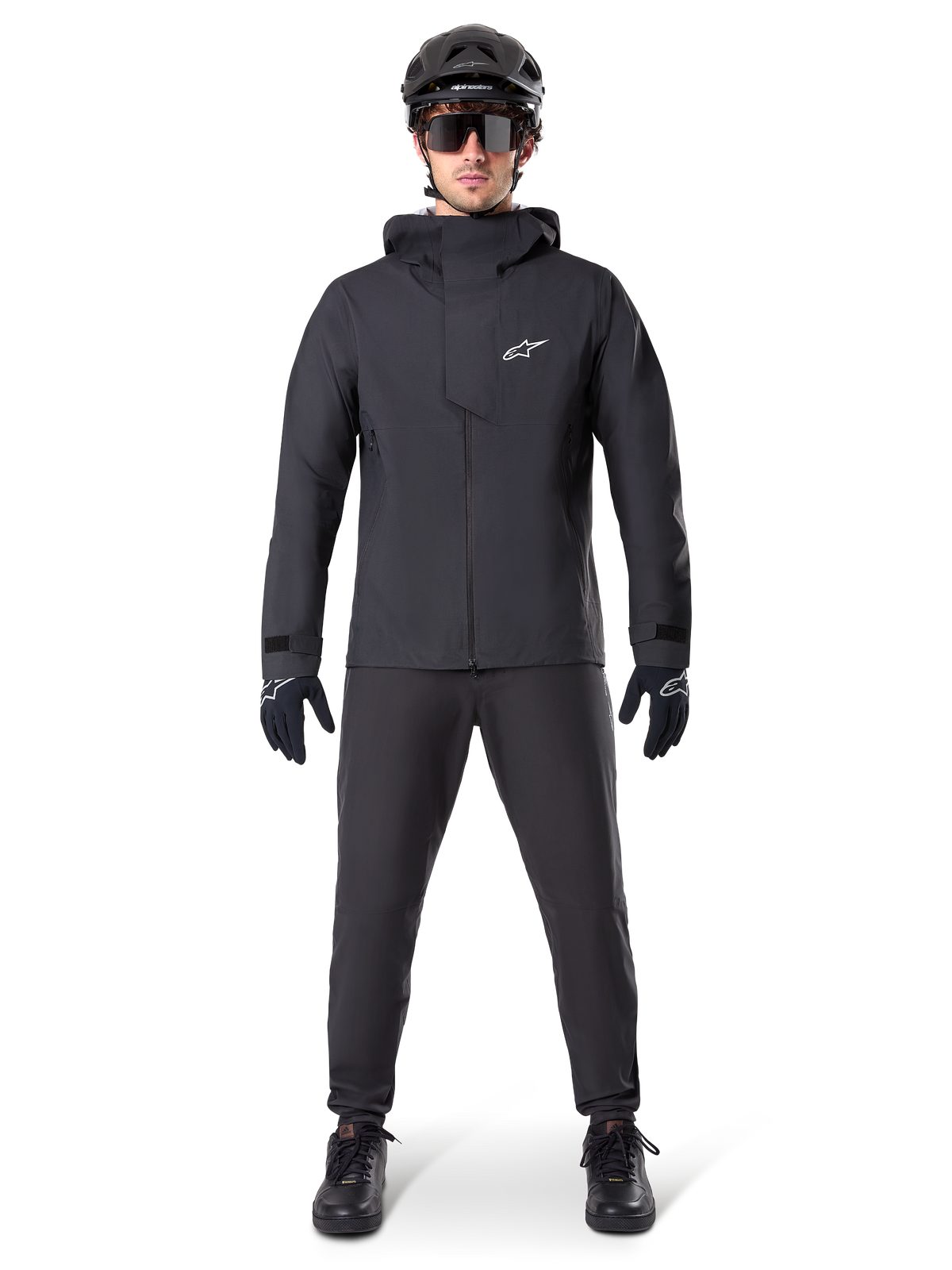 Alpinestars A-Dura Elite Wasserdichte Jacke, Schwarz, getragen mit passender Fahrradhose und Handschuhen, schwarzer Helm und Sonnenbrille, mit weißem Astars-Logo auf der Brust, leistungsstarkes technisches Design für Mountainbiking