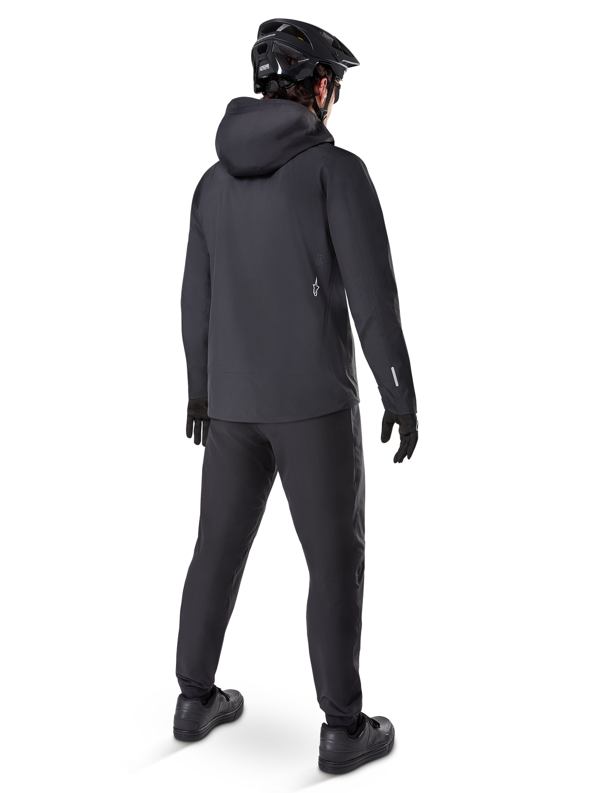 Alpinestars A-Dura Elite Wasserdichte Jacke, Schwarz, Rückansicht mit Über-dem-Helm-Kapuze und längerem, abfallendem Saum, kombiniert mit passender schwarzer MTB-Hose, Handschuhen und Helm für kompletten Allwetterschutz auf dem Trail.