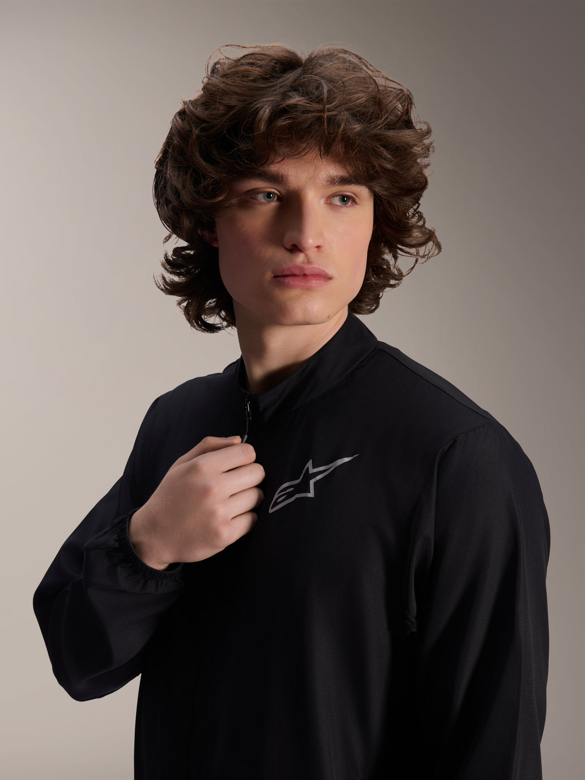 Alpinestars A-Aria Windbreaker Jacke, schwarze Radjacke, getragen von einem männlichen Model, Stehkragen-Design mit silbernem Astars-Logo auf der Brust, leichte und windabweisende Performance-MTB-Ausrüstung