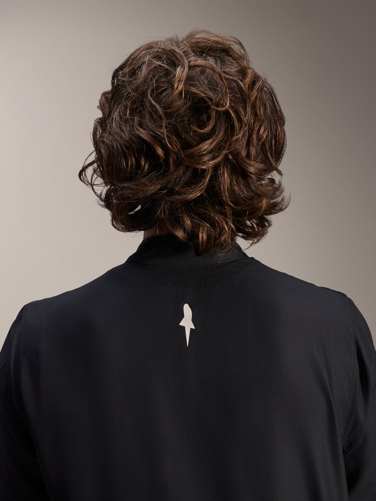 Alpinestars A-Aria Windbreaker Jacke, Schwarz, Nahaufnahme der Rückenansicht von Schultern und Kragen, mit einem kleinen weißen Logo in der Mitte des Rückens, getragen von einem Model mit welligem braunem Haar, minimalistische Performance-Radbekleidung