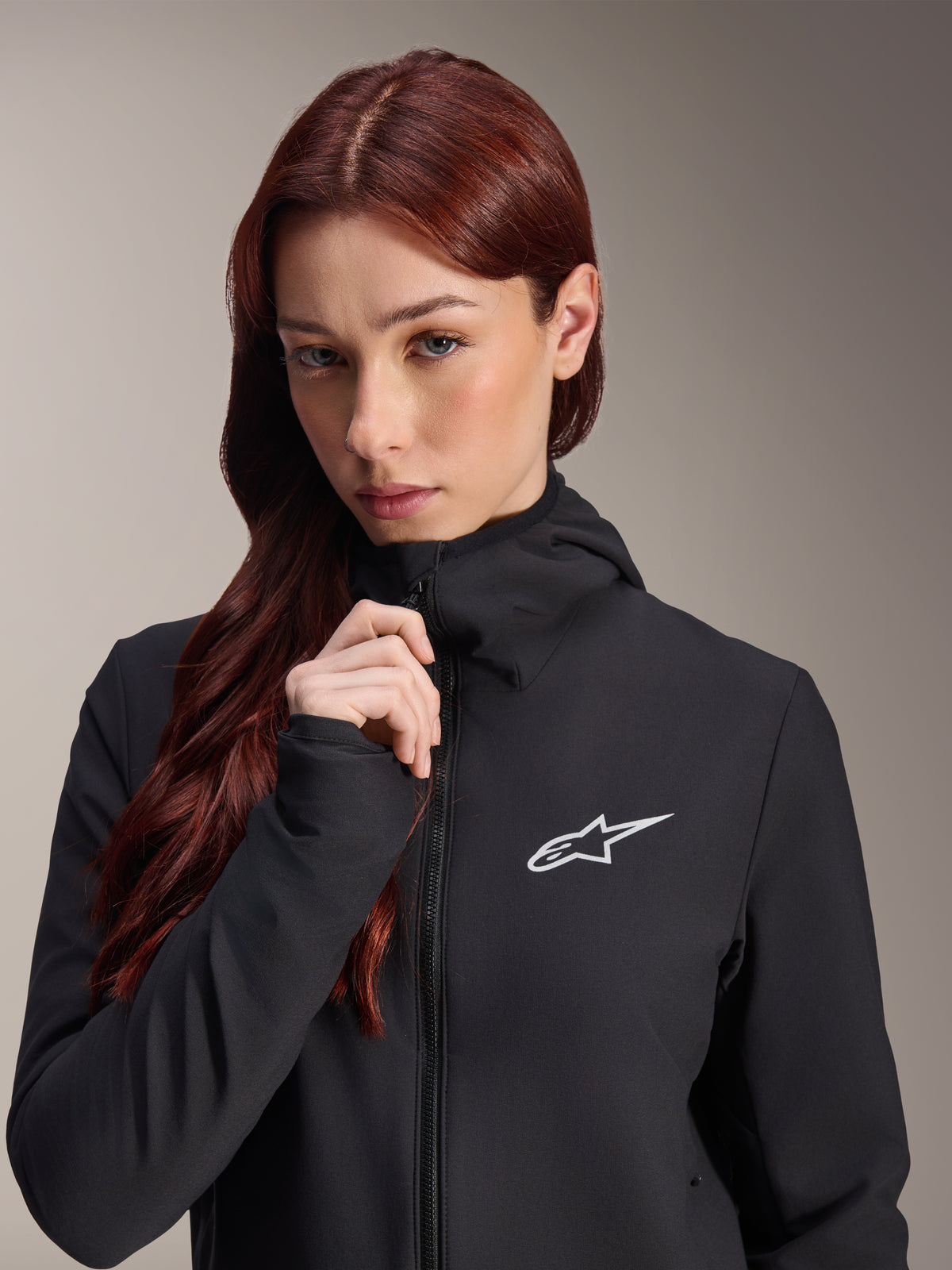 Alpinestars Stella A-Dura Thermal Jacket, Women's Black cycling jacket, worn by a model with long reddish-brown hair, white Alpinestars logo on the chest, hooded design with full-zip front, mountain bike apparel