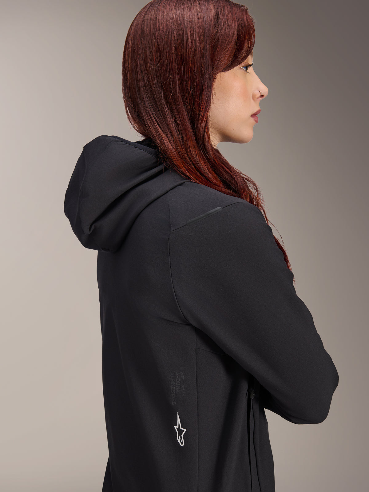 Alpinestars Stella A-Dura Thermal Jacket, Women's Cycling Jacket, Black, side profile of a woman with red hair wearing the jacket, features an integrated hood and white Alpinestars star logo on the side, lightweight insulated thermal gear for MTB.