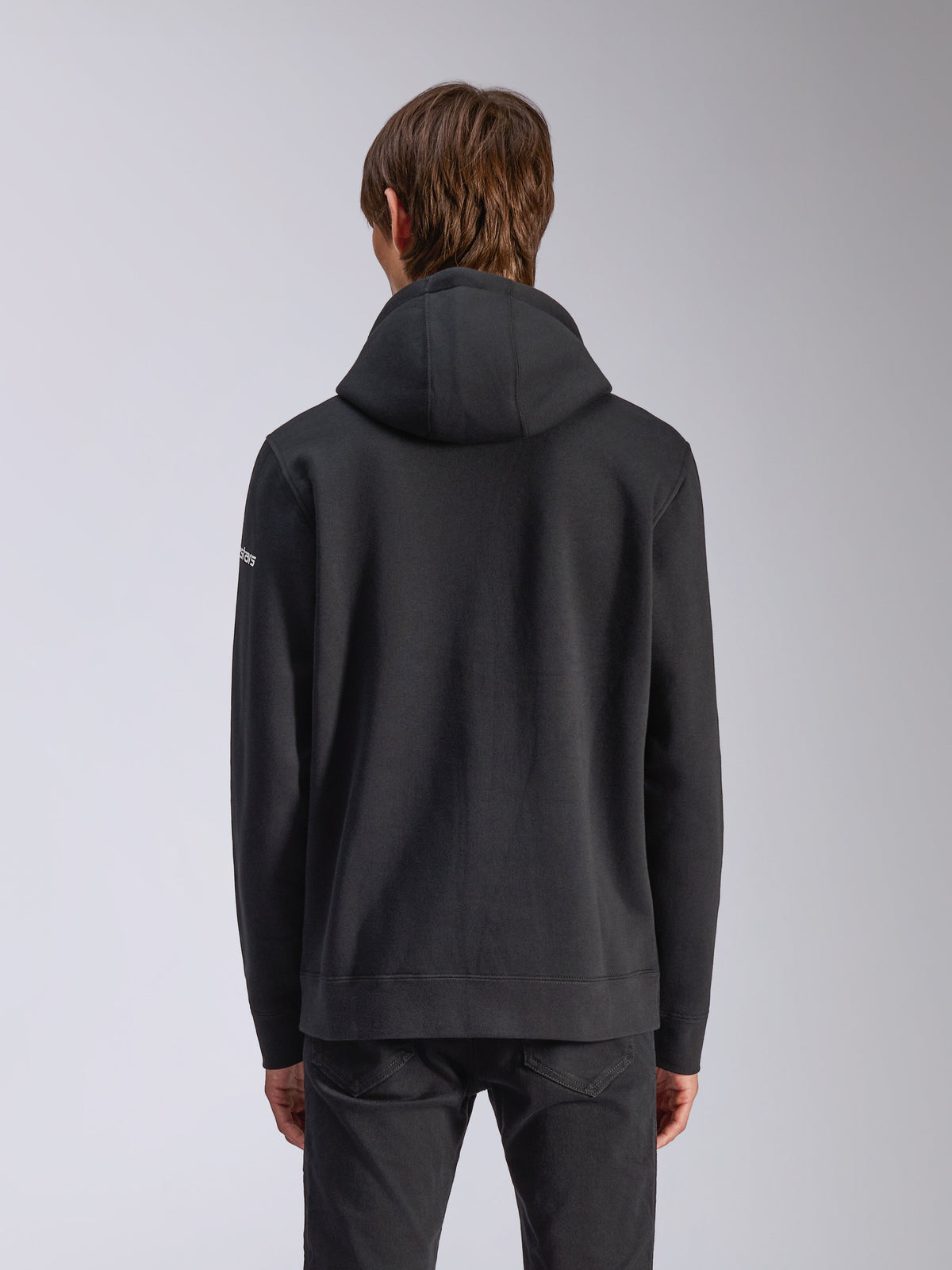 Alpinestars Frontal Hoodie, Black, back view of a casual pullover sweatshirt, featuring a self-lined hood, ribbed hem, and white wordmark logo on the sleeve, motorsport-inspired streetwear.