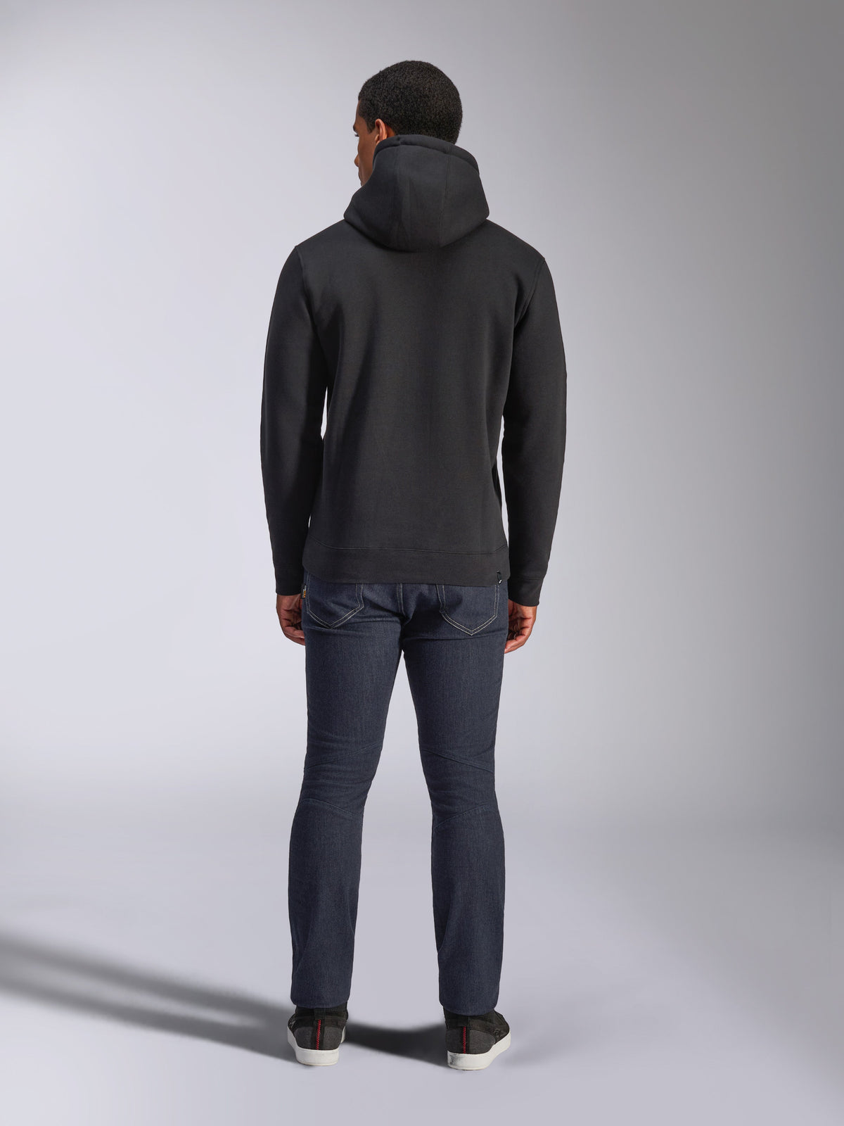 Alpinestars Blaze V3 Hoodie, casual streetwear, black, back view of hooded fleece sweatshirt, worn with dark blue denim jeans and black shoes, clean motorsport-inspired design