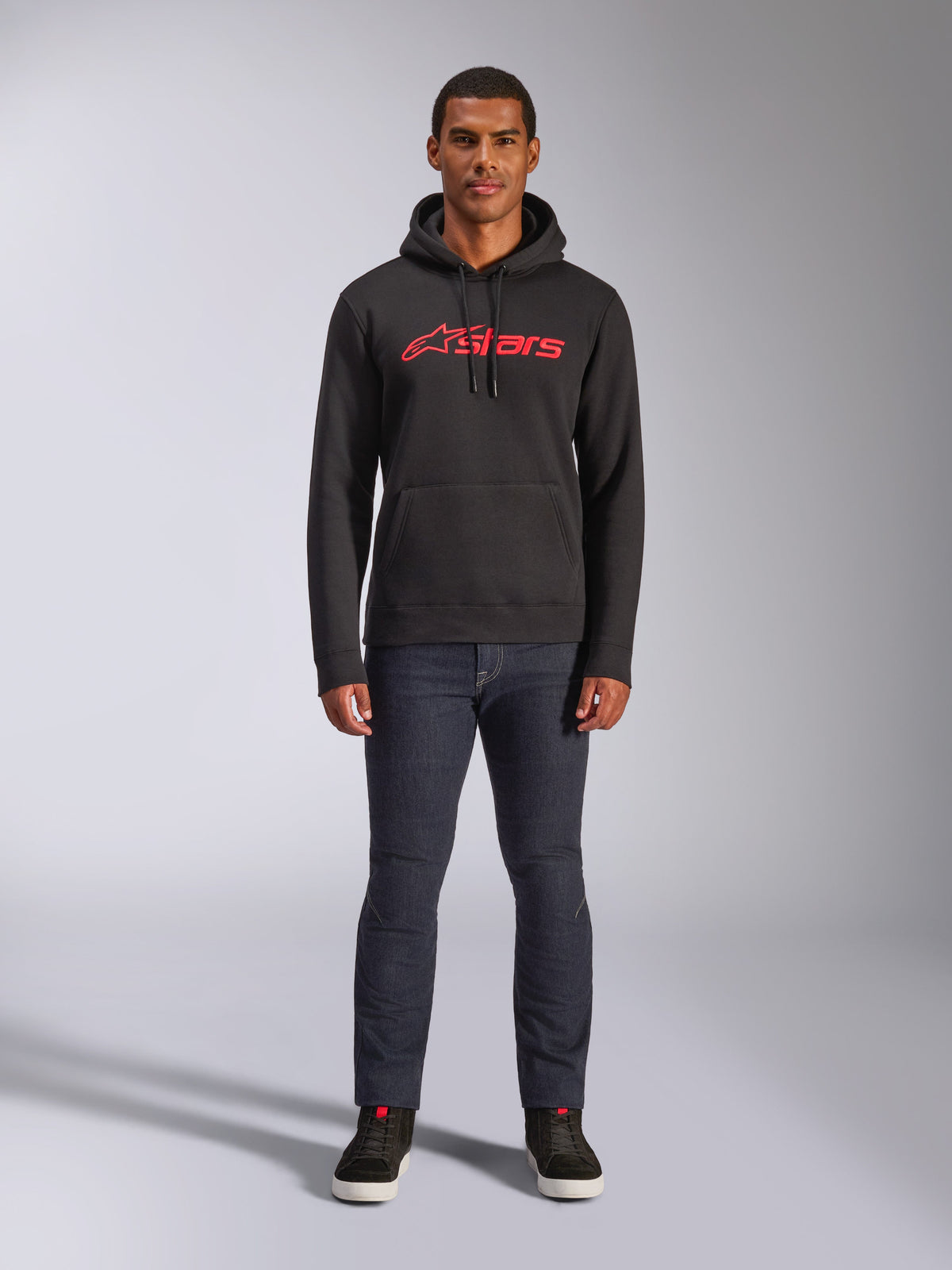 Alpinestars Blaze V3 Hoodie, casual streetwear, Black with Red Astars logo, front view, worn by model with dark denim pants and black sneakers, modern motorsport-inspired fleece design