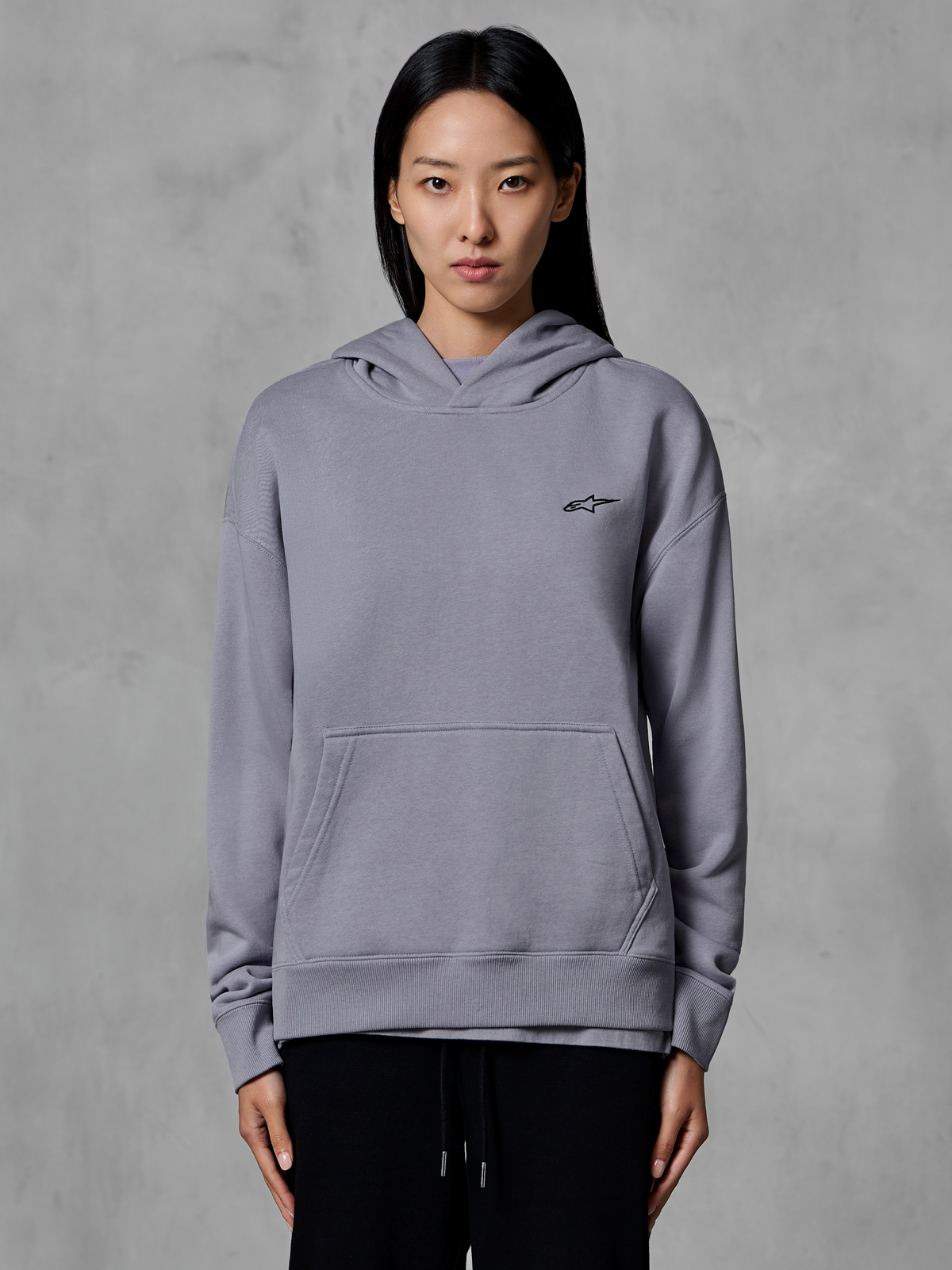 Alpinestars Essentials Ageless Hoodie, lässige Sportbekleidung, Silber mit kleinem schwarzem Logo, Kängurutasche, Kapuzenpullover, von einem Model getragen, moderne Lifestyle-Bekleidung