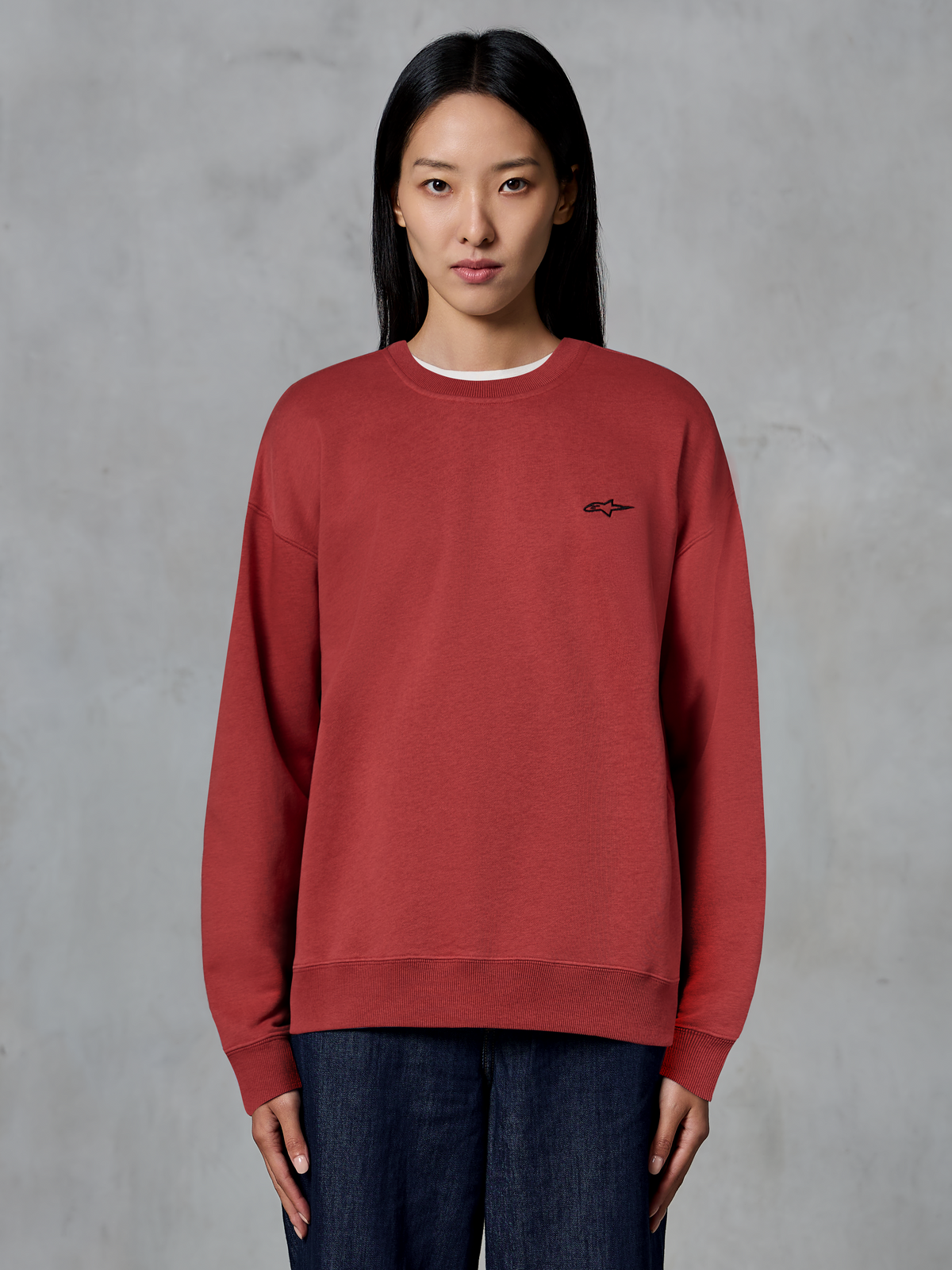 Alpinestars Essentials Ageless Crew, Rundhals-Sweatshirt in Brick Red, kleines schwarzes Logo auf der Brust, hochwertiges Fleece, getragen von einem Model, lässige Motorsport-inspirierte Streetwear