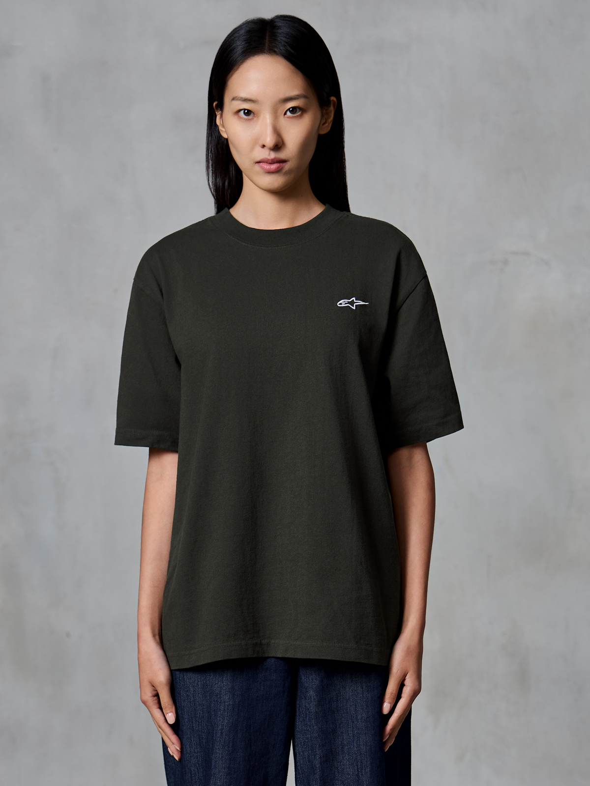 Alpinestars Essentials Ageless SS Tee, Kurzarm-T-Shirt, Off Black, getragen von einem weiblichen Model, entspannte Passform mit einem kleinen weißen Alpinestars-Logo auf der linken Brust, lässige Lifestyle-Bekleidung