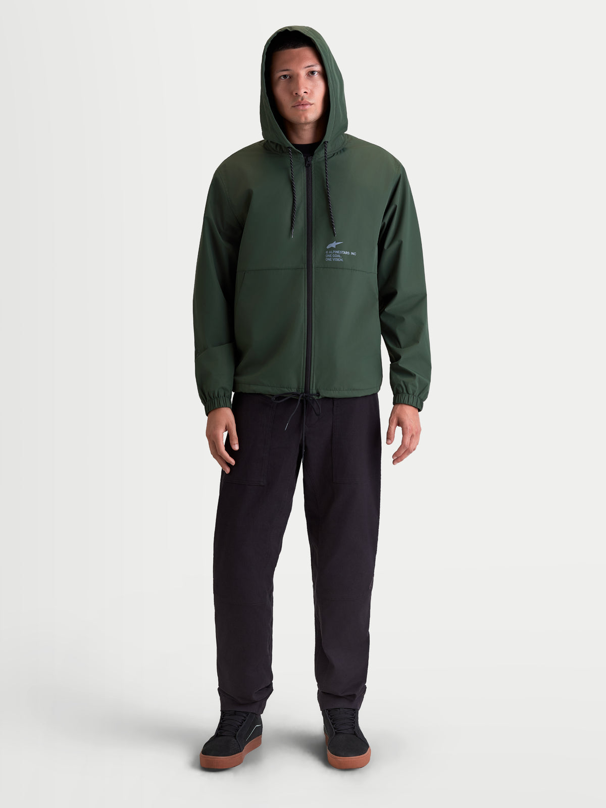 Alpinestars Speeder Resolve Winddichte Jacke, leichte Sportswear-Kapuzenjacke für Herren und Damen, Grün, 100 % Polyester, mit verstellbarer Kapuze, umgekehrtem Spiralreißverschluss und Alpinestars-Branding auf der Brust, Vorderansicht am Model.