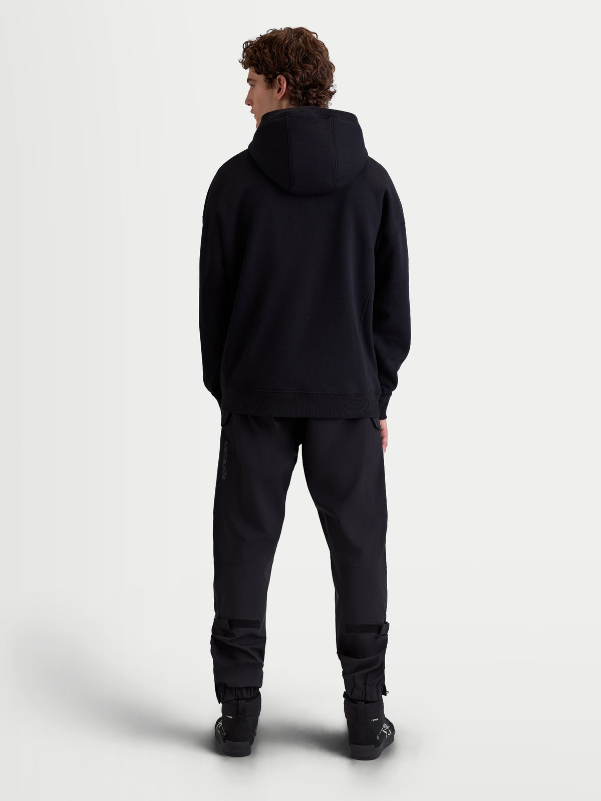 Alpinestars Shaw Oversize-Hoodie, lässiger Sportswear-Pullover, Rückansicht am Model in voller Länge, Schwarz, entspannte Silhouette mit gefütterter Kapuze und Rippbündchen, weiches Fleece-Material.
