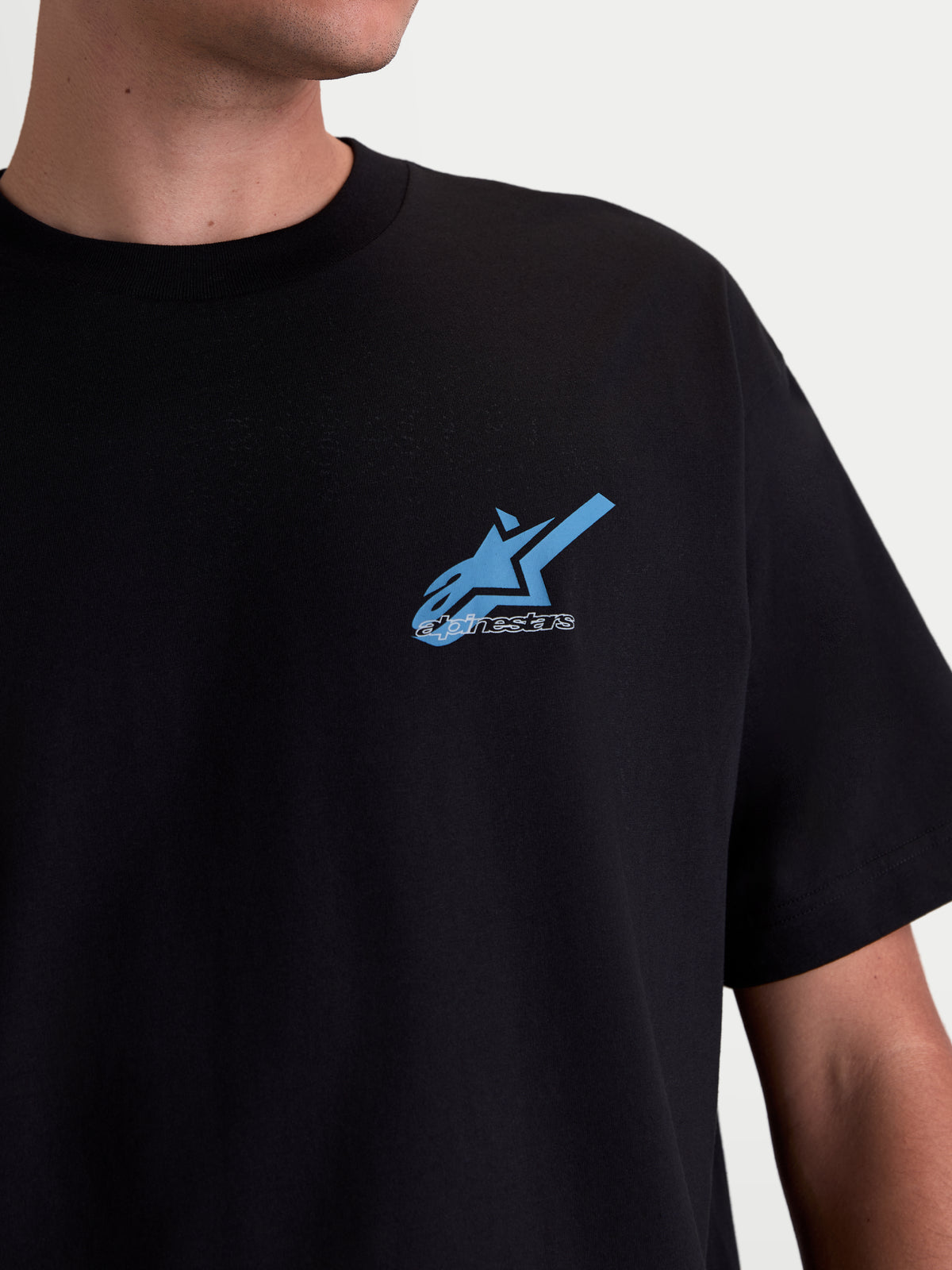 Alpinestars Ghost Oversized CSF T-Shirt, Kurzarm-Sportswear-T-Shirt, Schwarz mit blau-weißer Astars-Logo-Grafik auf der Brust, Premium-Baumwoll-Polyester-Mischung, Nahaufnahme am Modell.