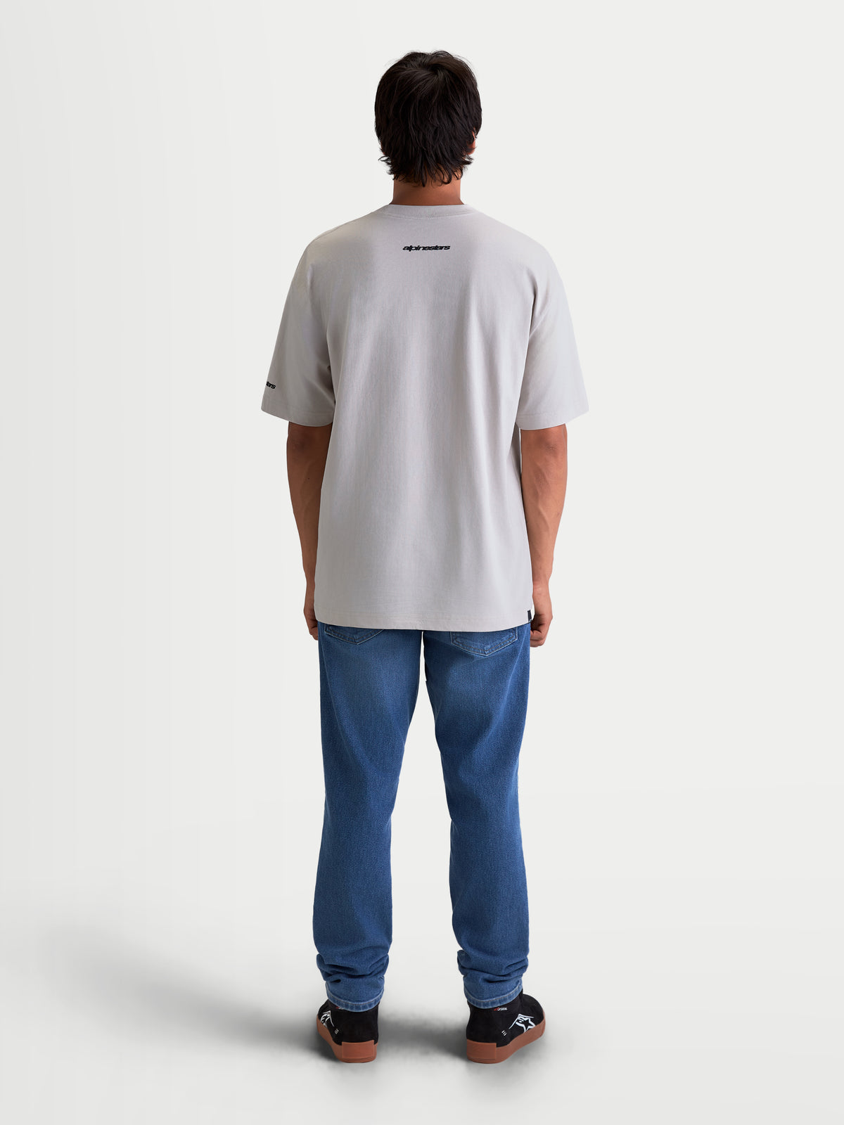 Alpinestars Mandate Oversized CSF T-Shirt, Kurzarm-Sportswear-T-Shirt, Unisex, Grau, Rückansicht am Model. Locker geschnittene Oversized-Passform mit schwarzer Alpinestars-Wortmarke auf dem oberen Rücken, aus weichem Baumwoll-Polyester-Mix für täglichen Tragekomfort.