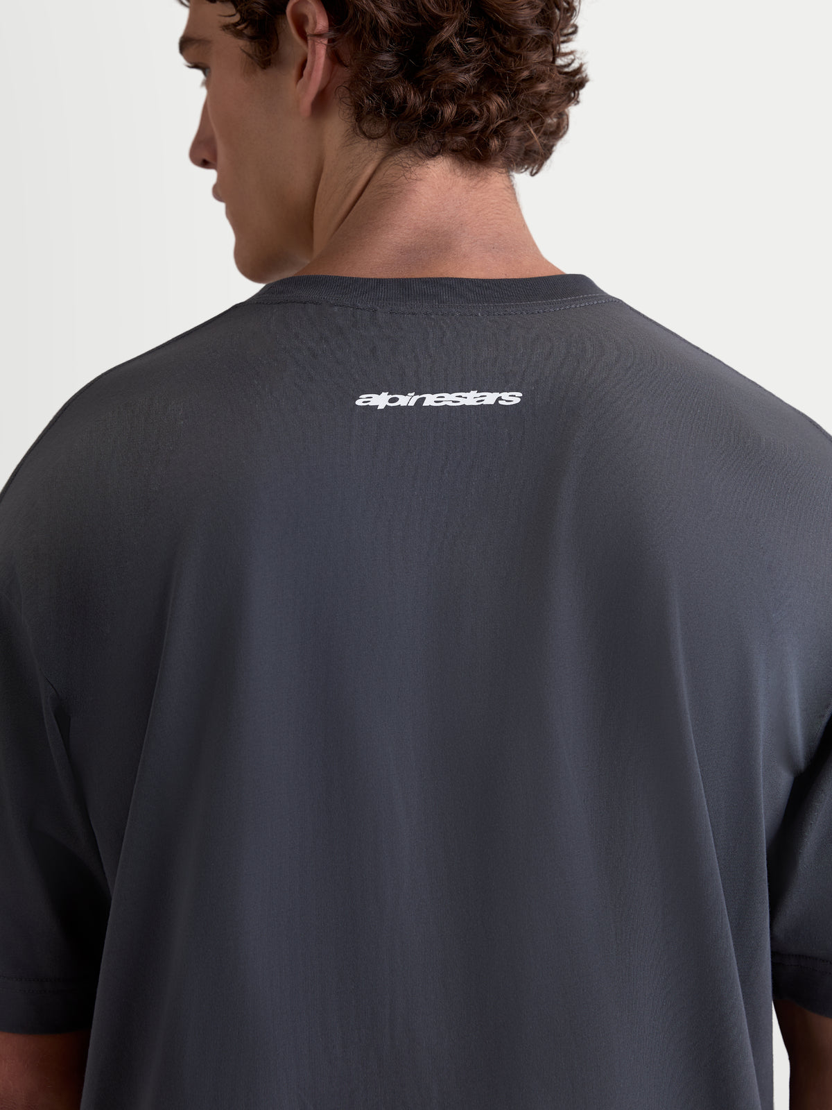 Alpinestars Prelude Oversized CSF T-Shirt, Kurzarm-Sportswear in Grau, Rückansicht am Modell mit weißem Alpinestars-Wortlogo auf dem Rücken, lockere Oversized-Passform, weicher Baumwoll-Polyester-Mix.