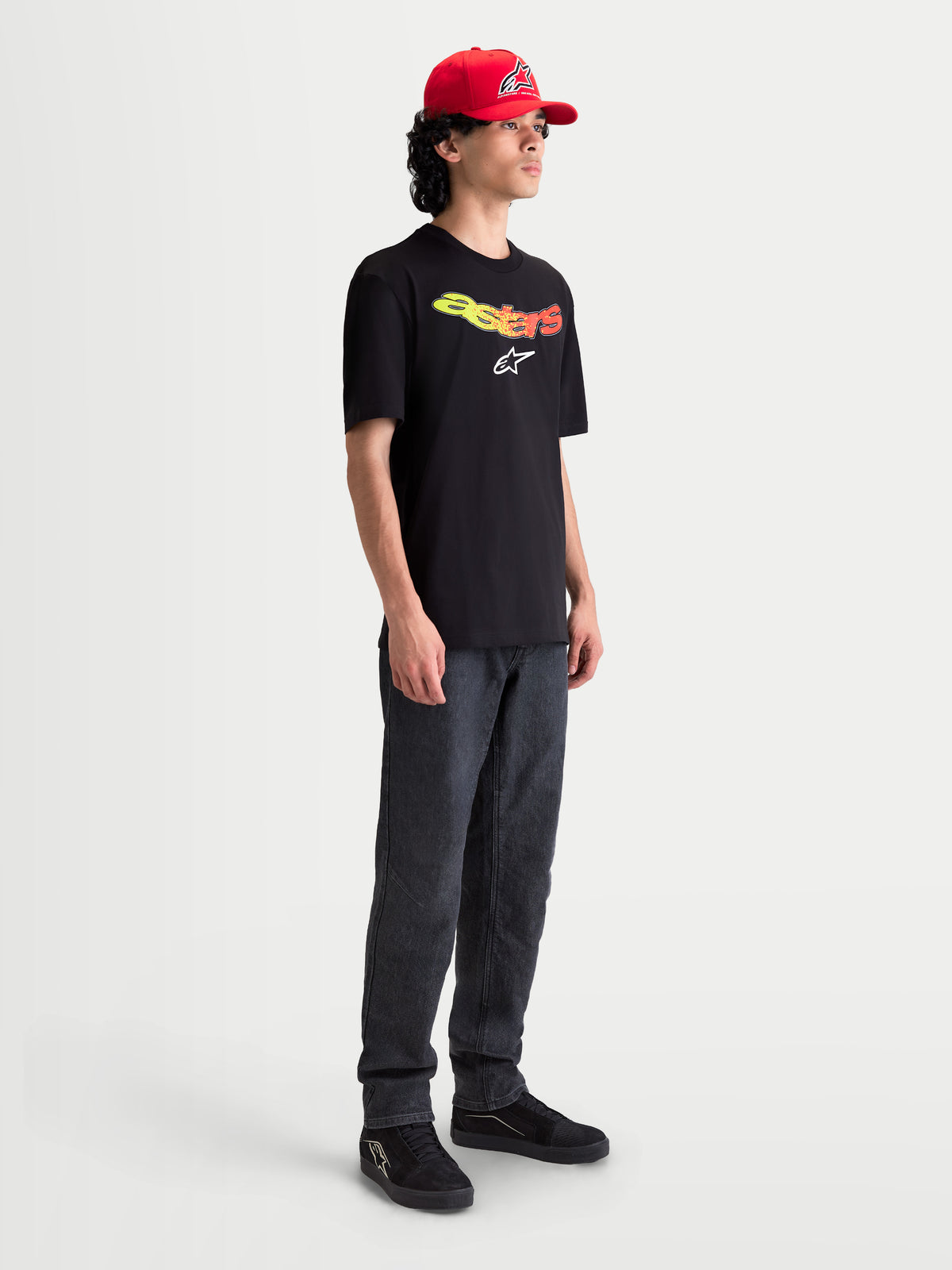 Alpinestars Elliptogrit CSF T-Shirt, Kurzarm-Sportswear-T-Shirt für Herren, Schwarz mit gelb-rotem Astars-Schriftzug im Farbverlauf und weißer Logo-Grafik, getragen von einem Model, lässiger Motorsport-Stil.