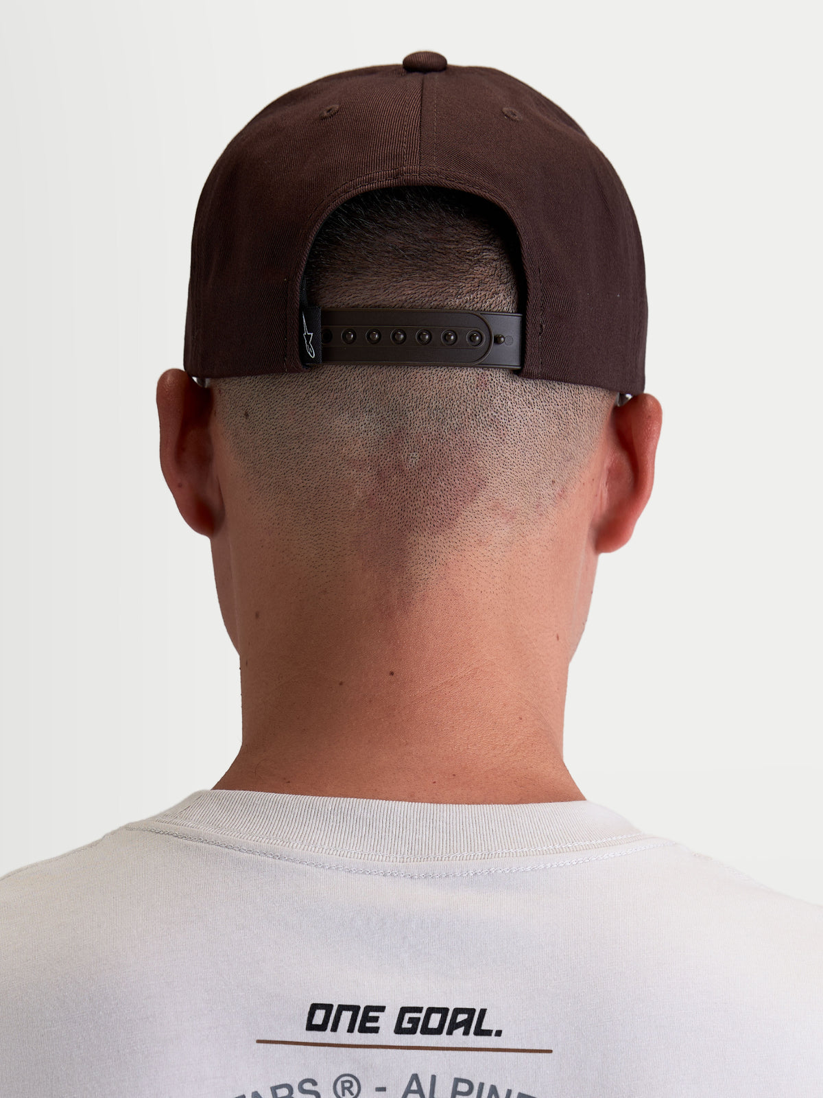 Alpinestars Combo Logo Snapback Kappe, Motorsport-Sportswear-Kappe für Herren und Damen, Braun, strapazierfähige Twill-Konstruktion, Rückansicht am Modell zeigt den verstellbaren Snapback-Verschluss und das Marken-Etikett.