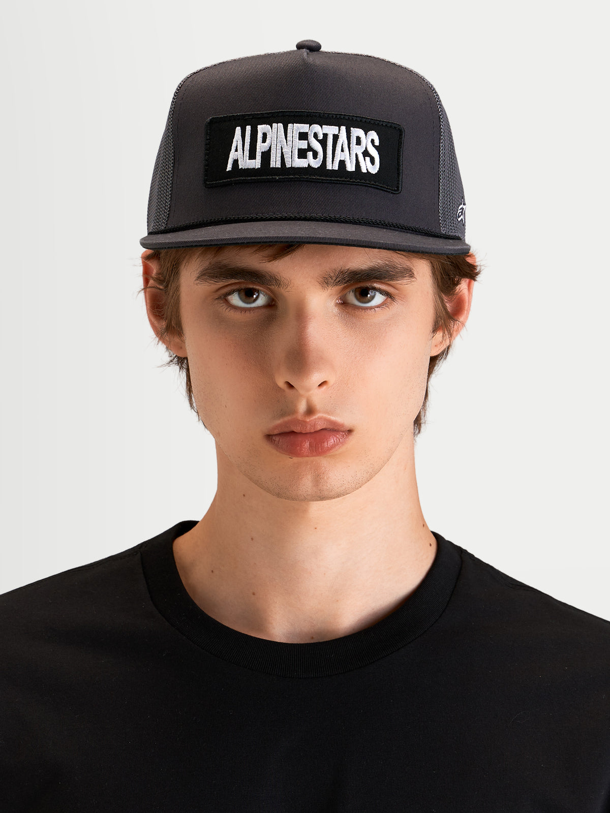 Alpinestars Ten Trucker-Kappe, flache Sportswear-Cap in Dunkelgrau, getragen von einem Model, mit strukturierter Krone und vorderem Alpinestars Wortlogo-Stickpatch