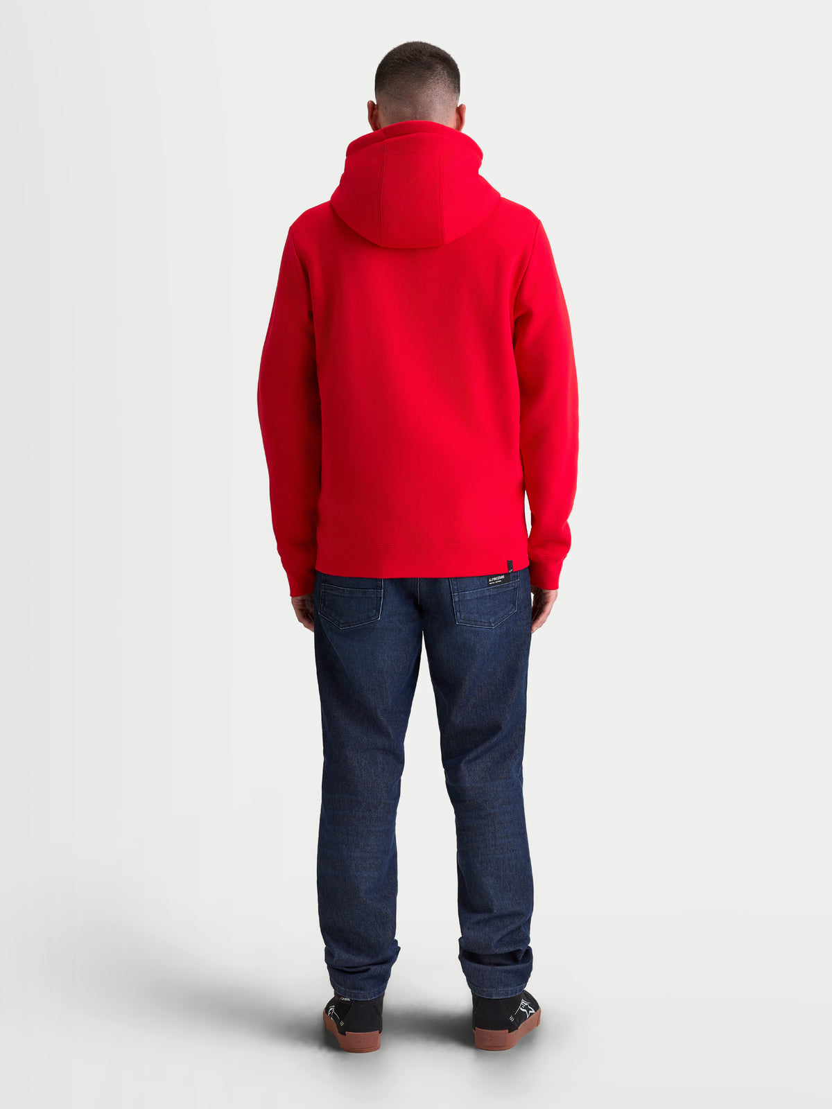 Alpinestars Ageless Zip V3 Hoodie, rote Sportswear-Fleecejacke für Herren und Damen, Rückansicht am Modell, mit bequemem Kapuzendesign sowie Rippbündchen an Ärmeln und Saum, lässiger Motorsport-Stil.