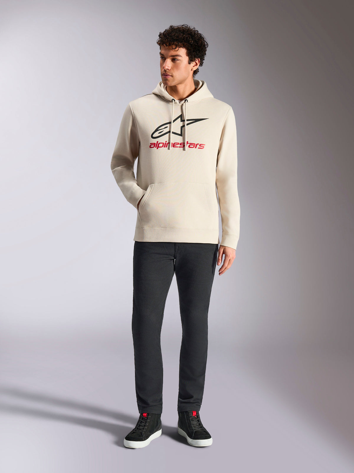 Alpinestars Always V3 Hoodie, lässige Streetwear, Off-White mit schwarzem Stern-Logo und rotem Schriftzug, Kapuze mit Kordelzug, lange Ärmel, getragen von einem männlichen Model mit schwarzer Hose und schwarzen Sneakern